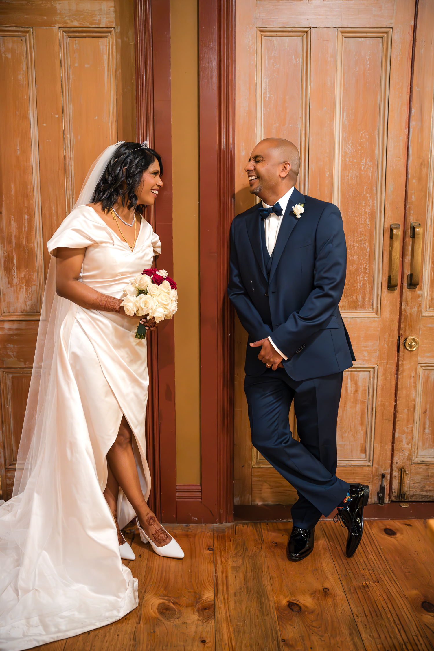 A couple in wedding attire share a playful moment against rustic wooden doors.