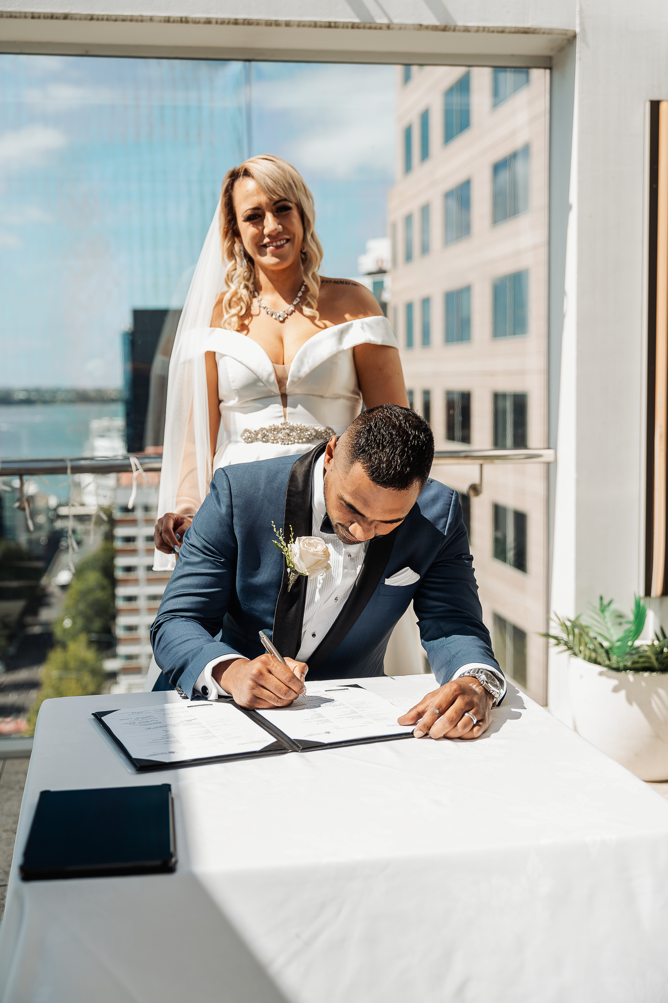 Couple signs marriage certificate on balcony overlooking cityscape.