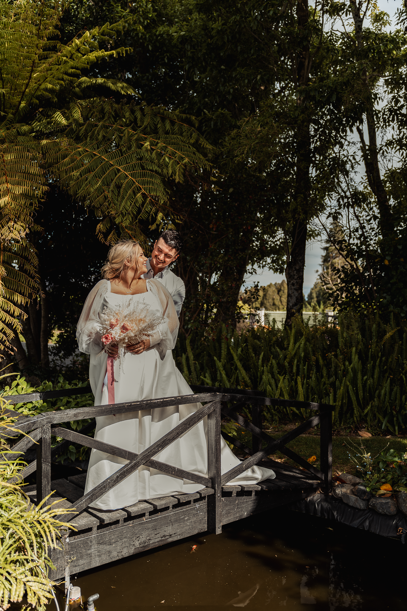 Wedding couple shares intimate moment on wooden bridge surrounded by lush garden foliage.