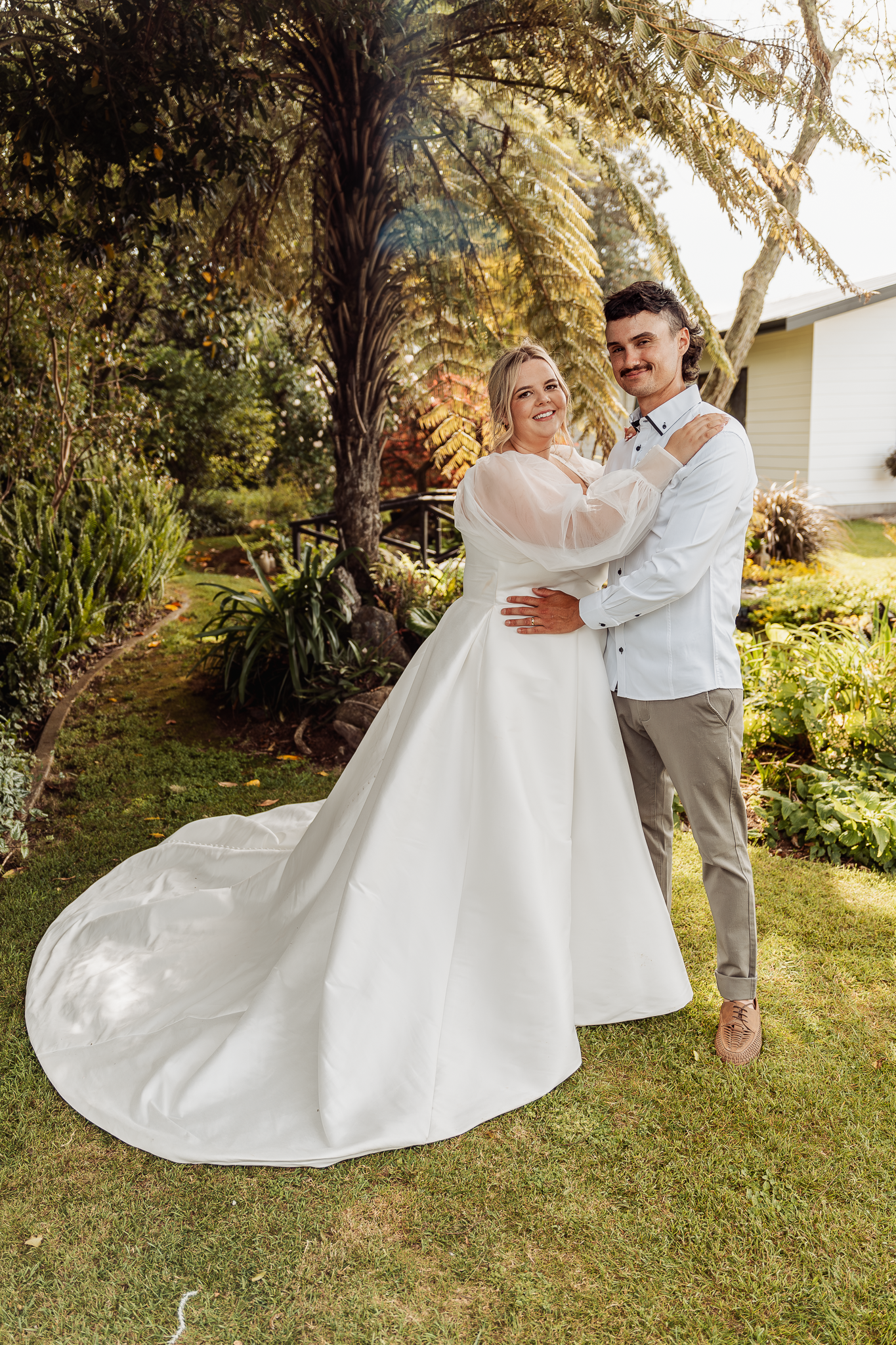 Dancing couple in wedding attire against garden backdrop with flowing white dress train.