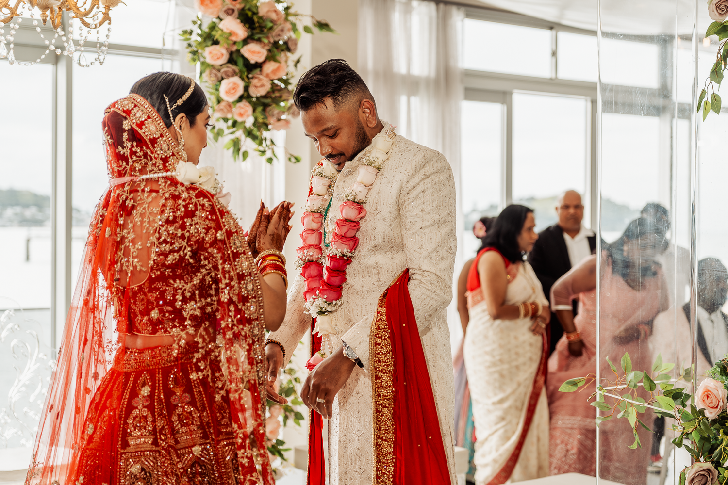 Traditional Indian wedding ceremony taking place in a bright venue with pink floral decorations.