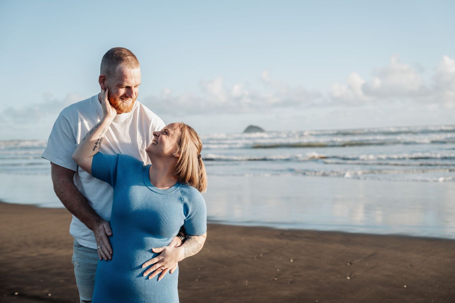A romantic moment captured on a beach with gentle waves and clouds in the background.