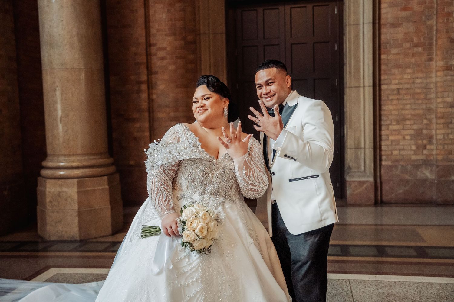 Bride and groom share intimate moment against brick wall backdrop in classic architectural setting.