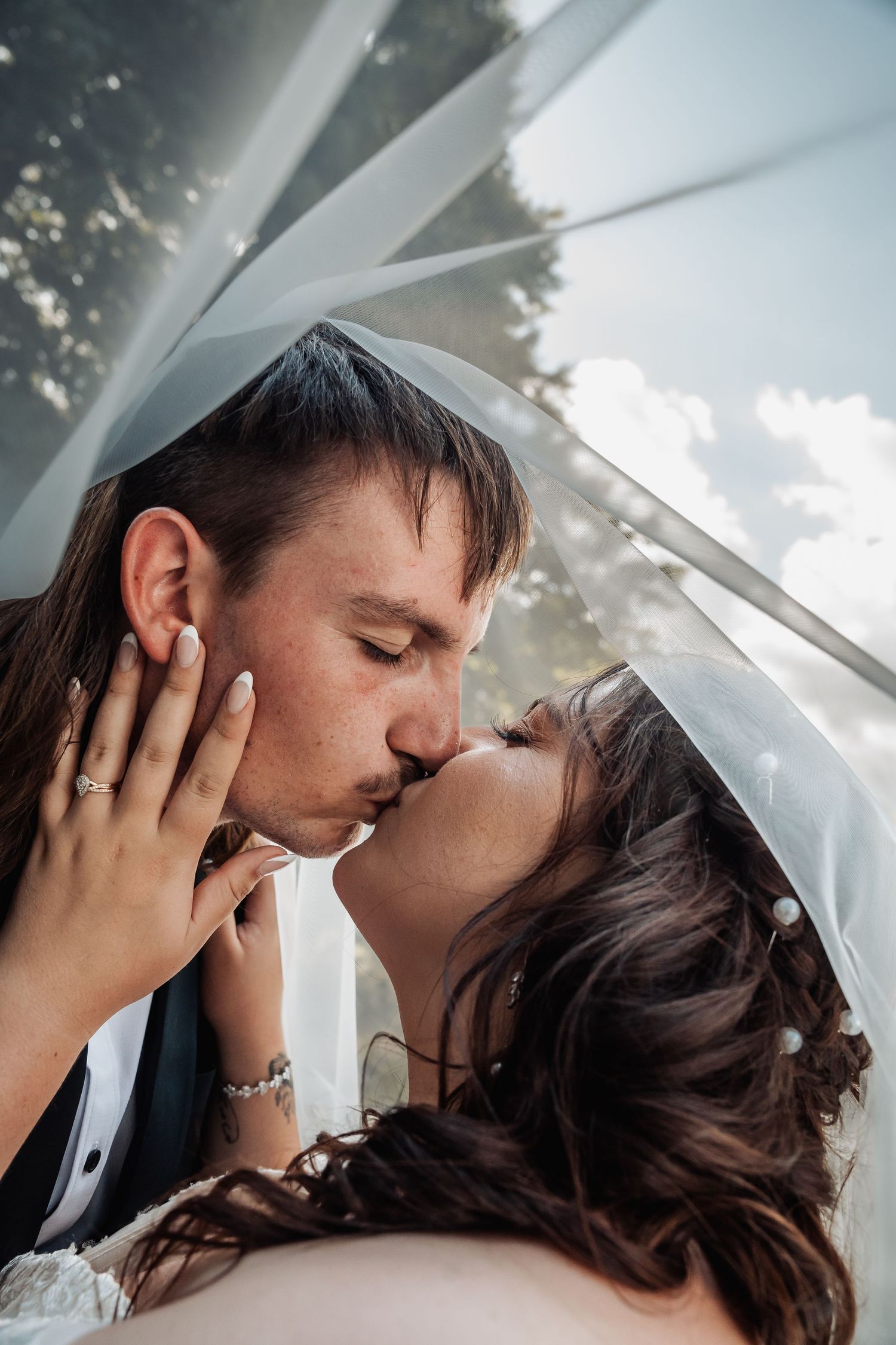 Bride and groom sharing a romantic kiss under a flowing white wedding veil.
