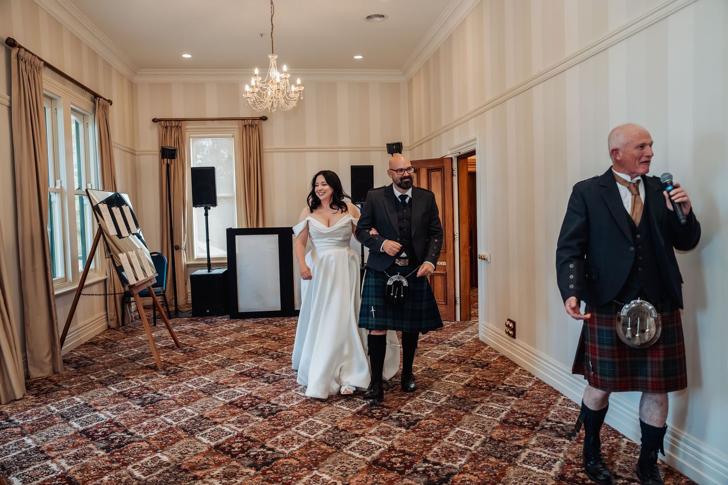 Bride and groom in Scottish kilt entering wedding reception hall accompanied by bagpiper.