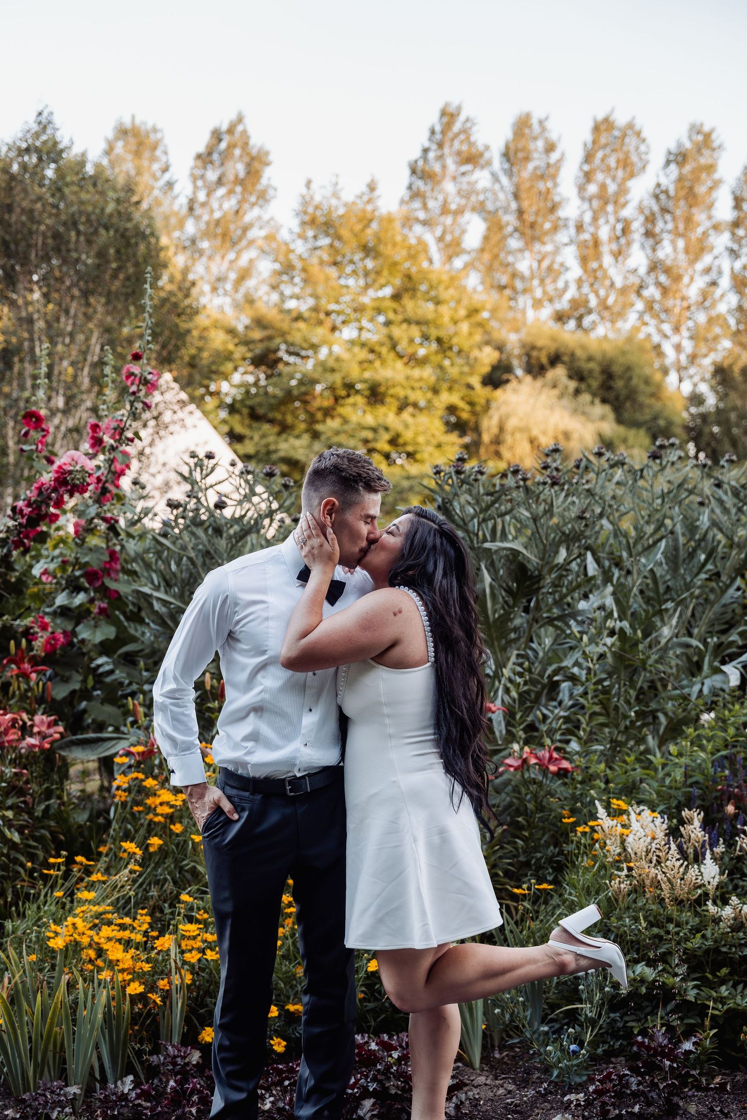Couple shares a kiss in a vibrant flower garden at golden hour.