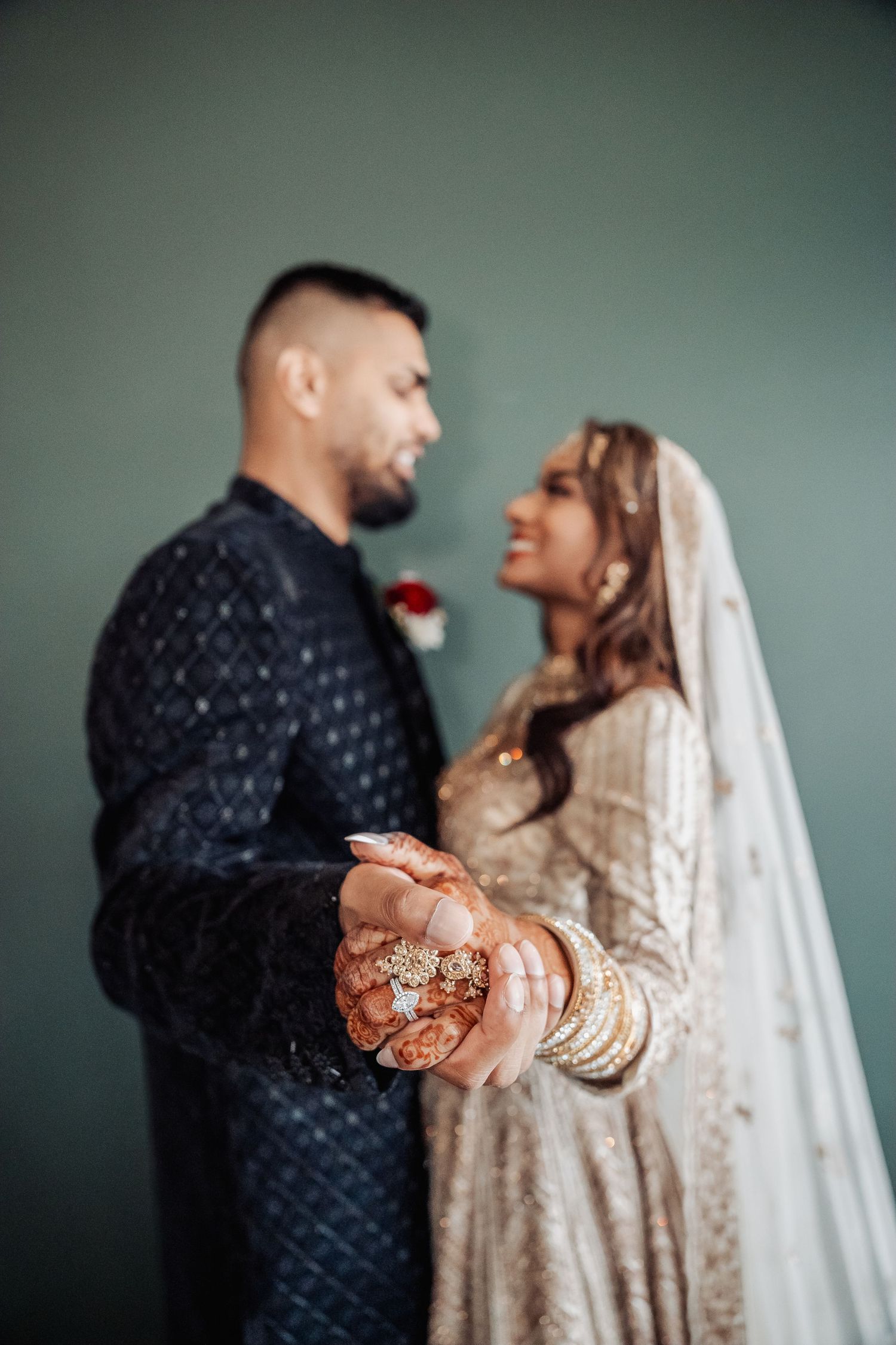 Couple in wedding attire sharing intimate moment against sage green wall.