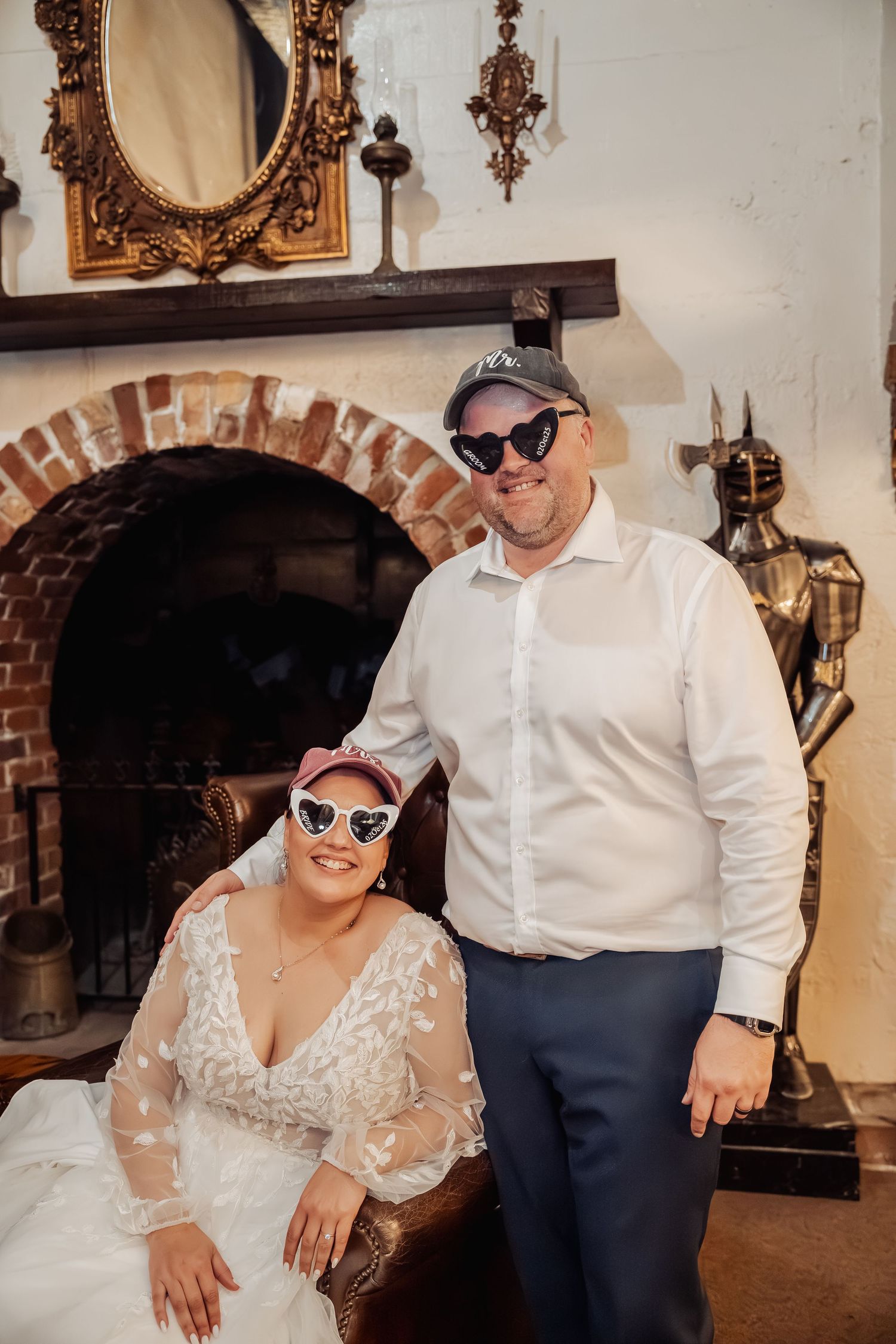 Wedding couple wearing matching sunglasses pose by a rustic brick fireplace.