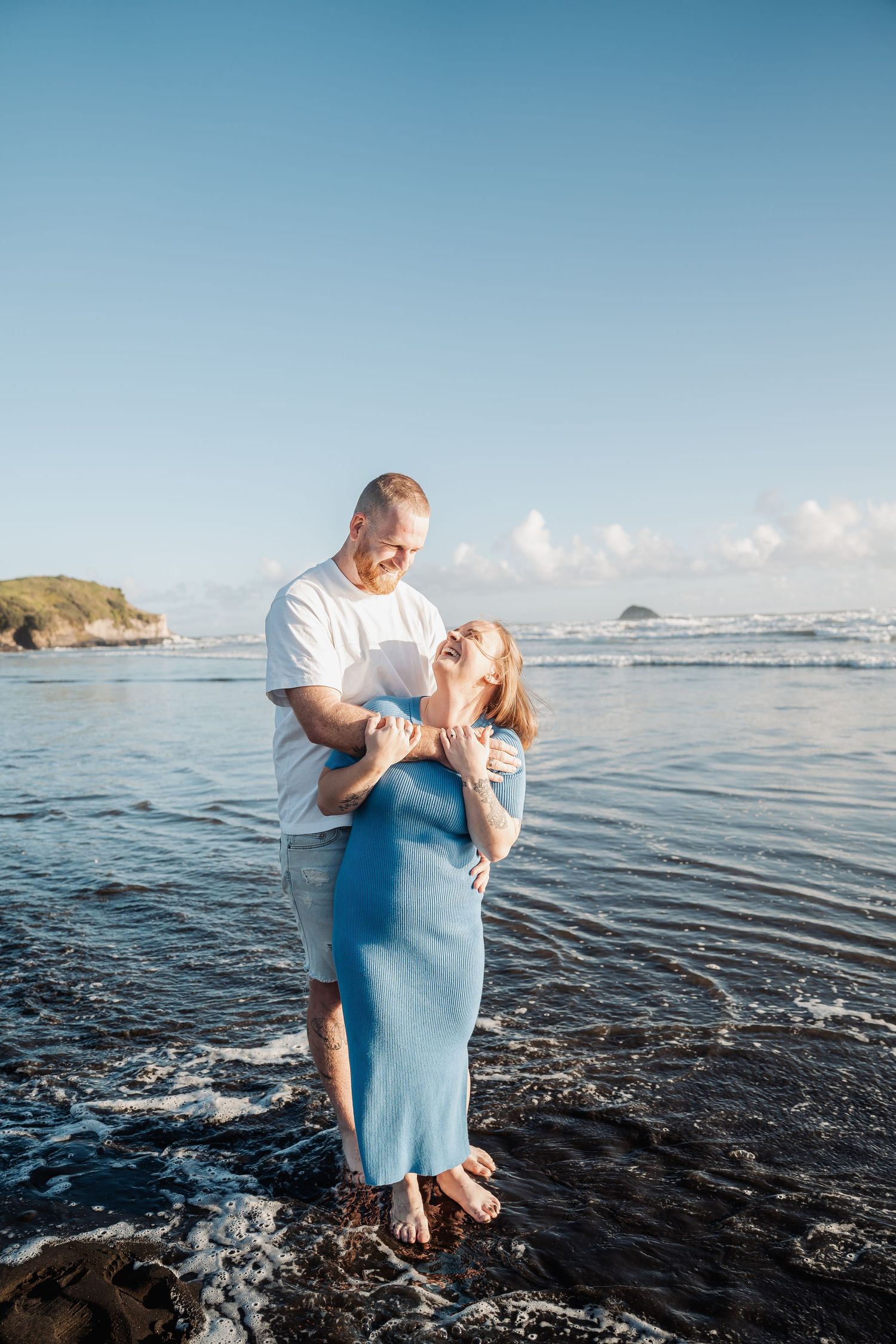 A romantic couple shares intimate moments while standing in shallow ocean water on a sunny day.