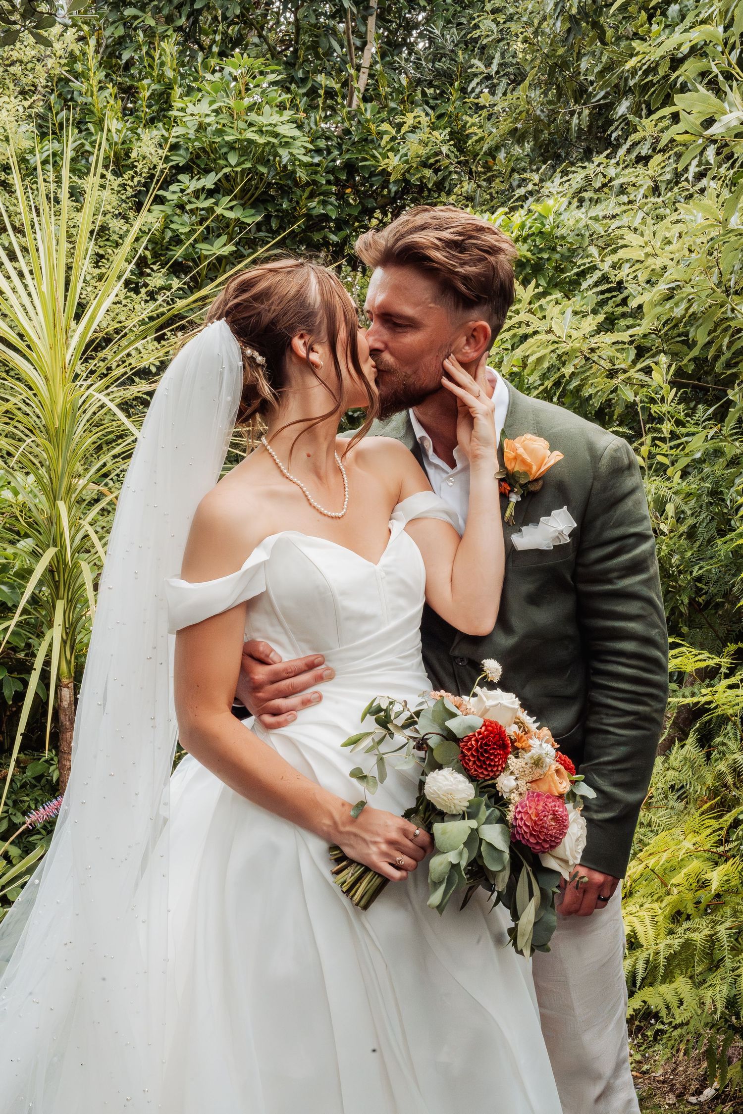 Bride and groom sharing a romantic kiss in a lush garden, bride holding a colorful bouquet.