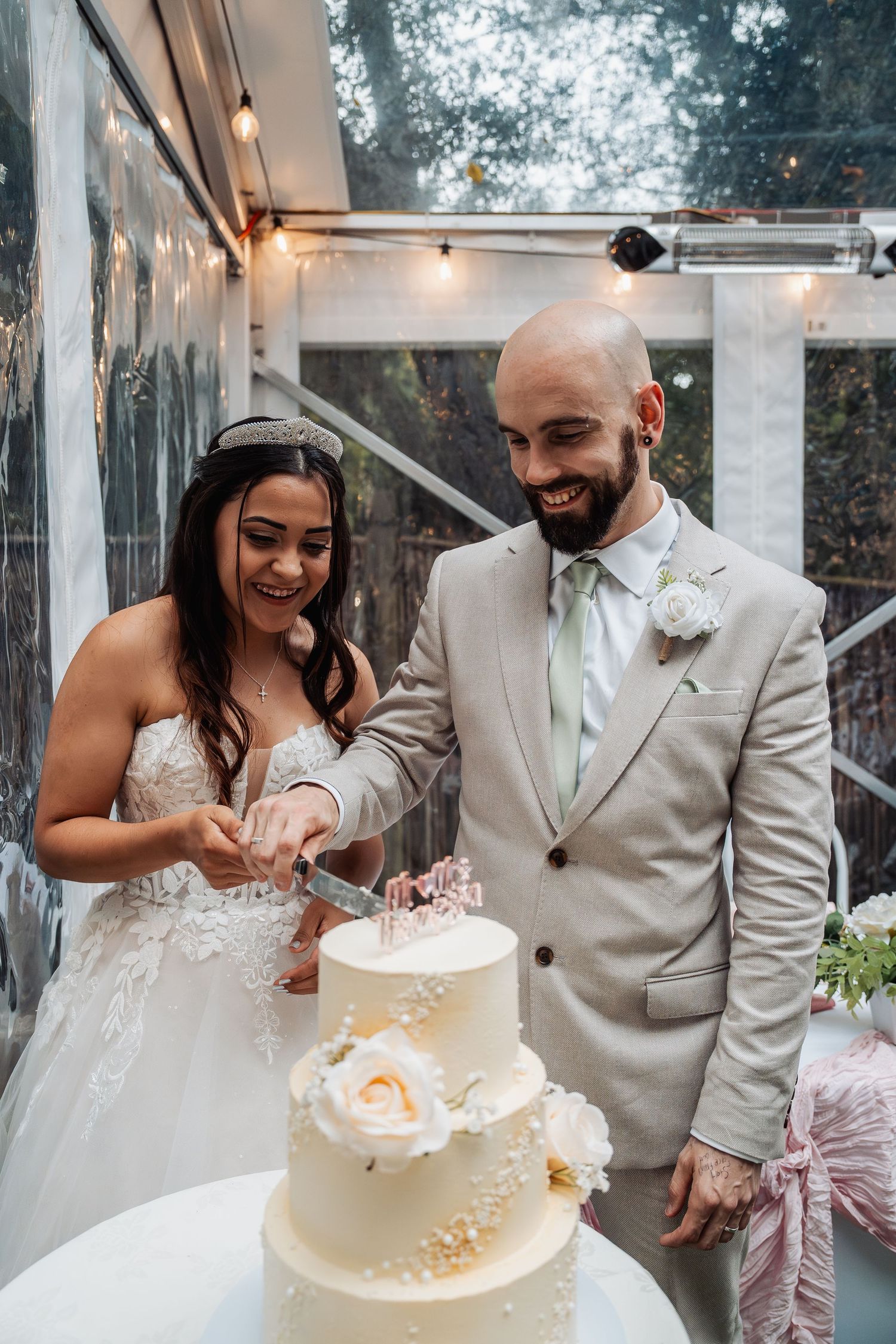 Happy bride and groom cut their elegant three-tier white wedding cake decorated with roses at their reception.