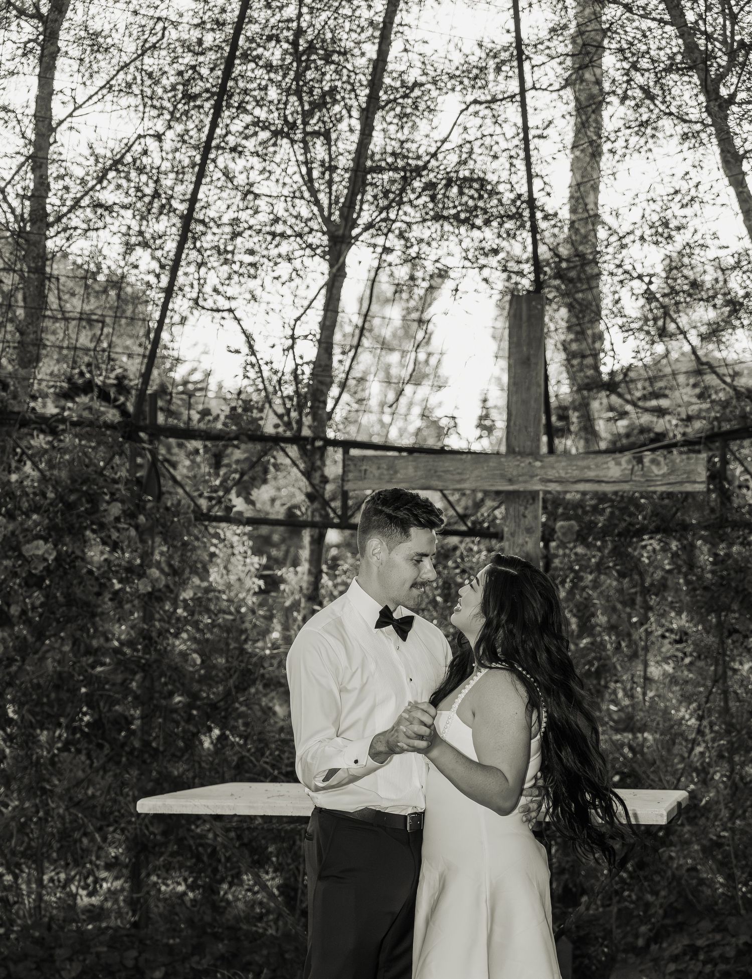 Black and white photo of bride and groom dancing romantically outdoors surrounded by trees.