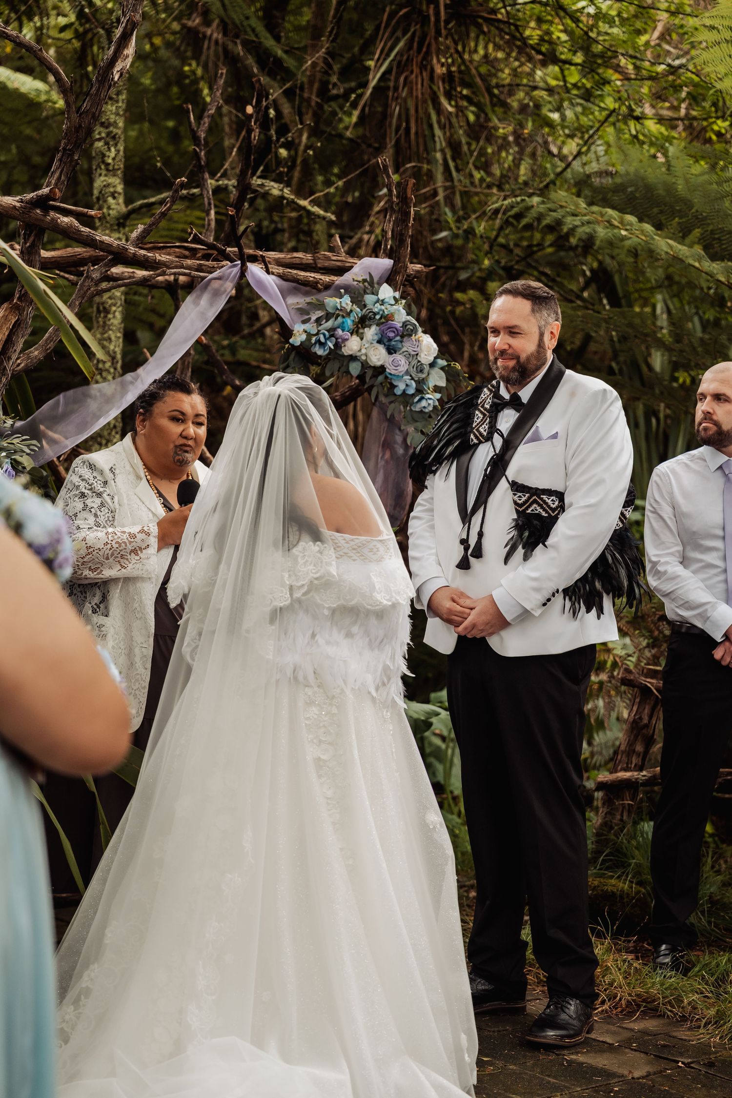 Bride and groom exchange vows at an outdoor woodland wedding ceremony with a floral arch backdrop.