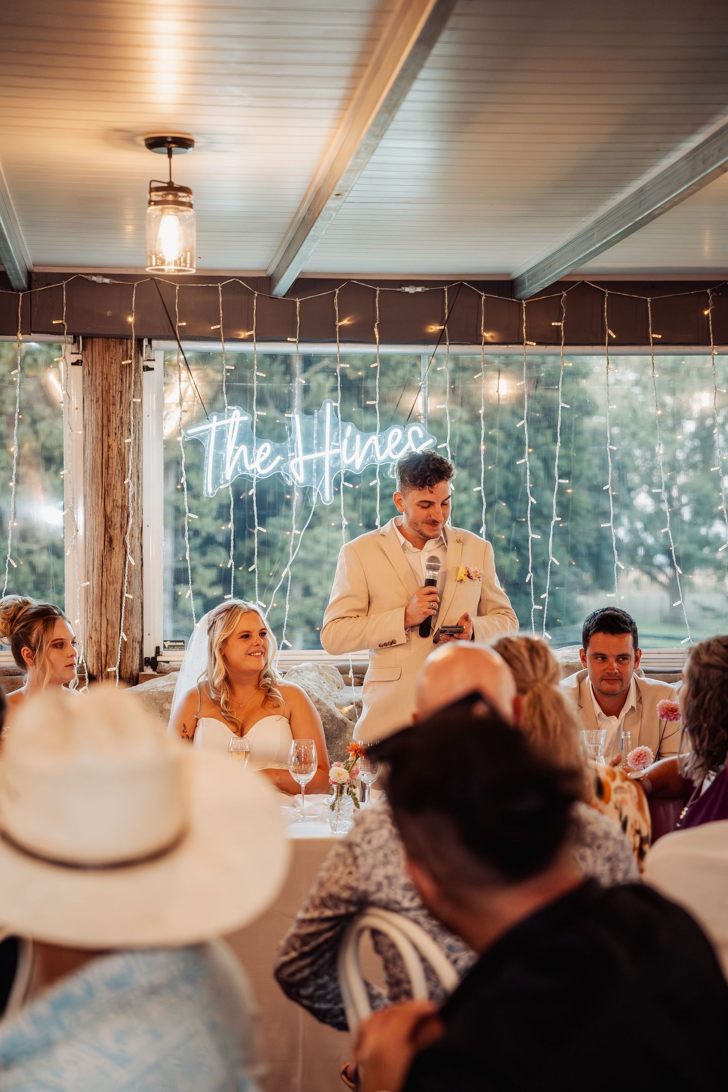 Groom delivers a heartfelt speech at wedding reception with neon sign reading The Hines glowing behind him.