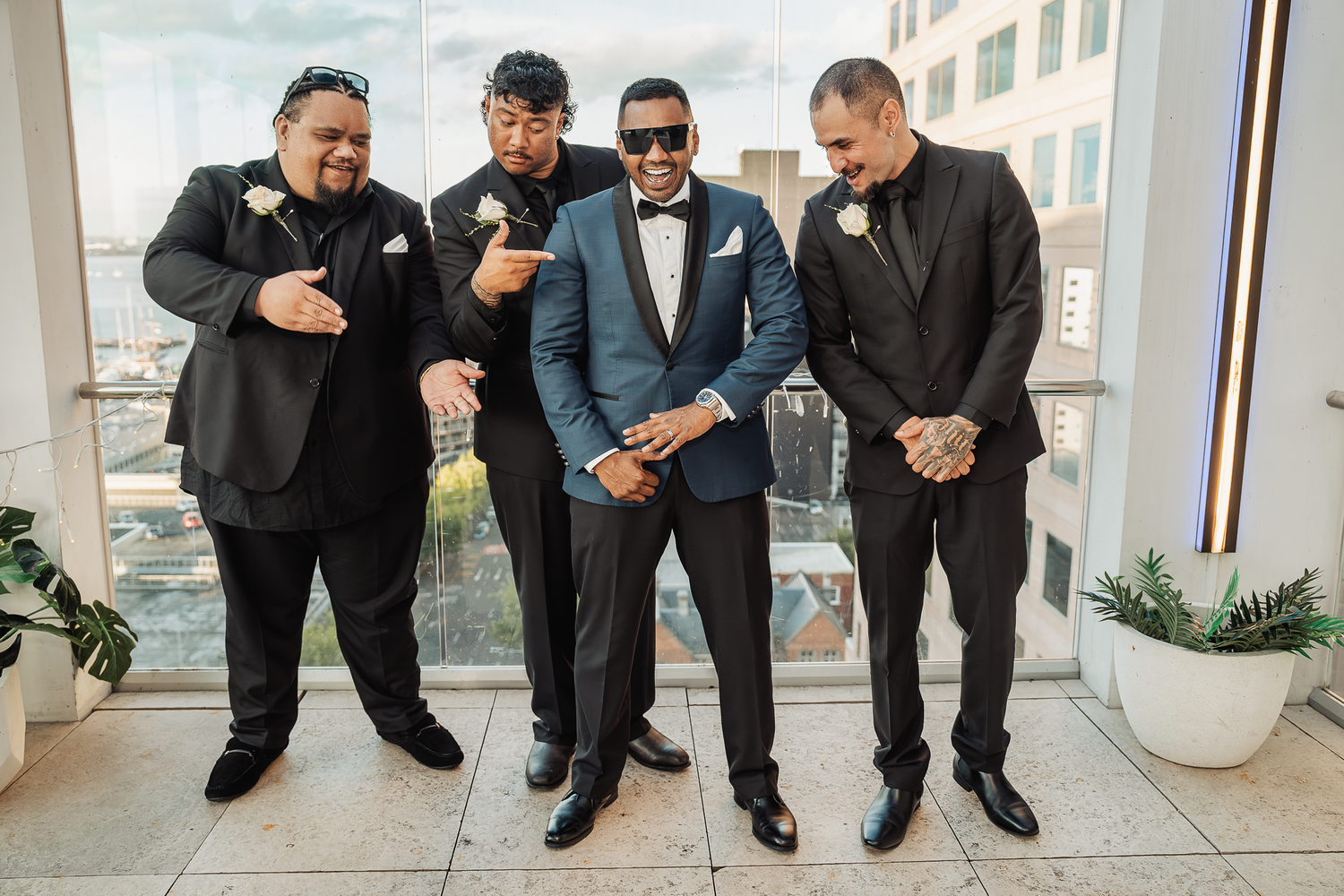 Groomsmen pose together in suits and sunglasses at a modern venue.