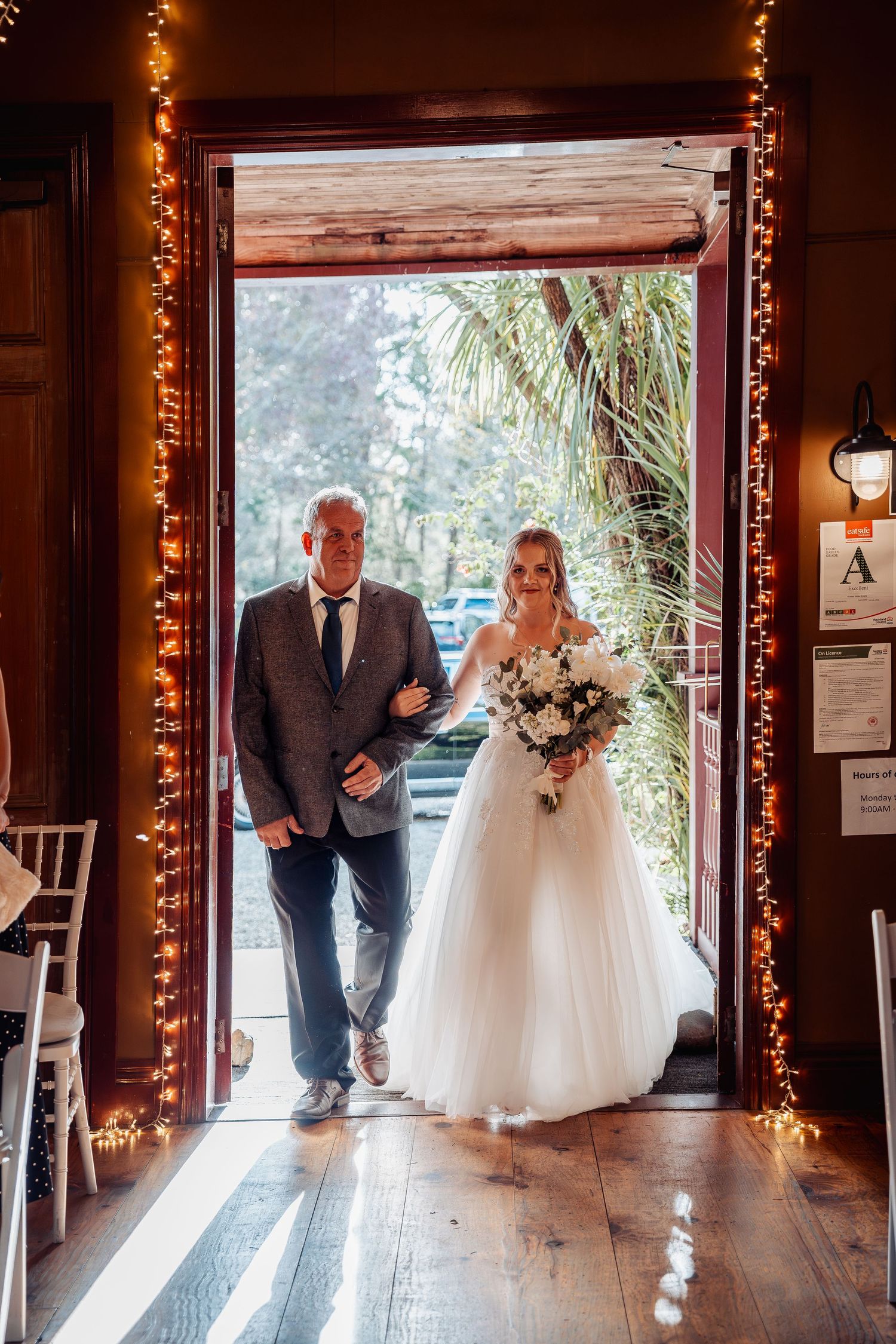 A romantic entrance decorated with warm string lights as pair enters rustic wedding venue.