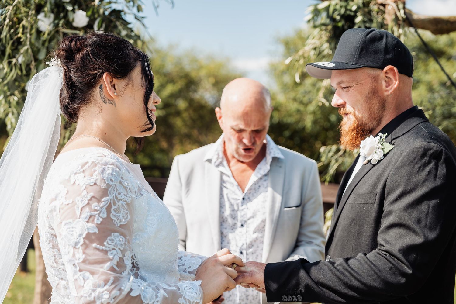 A couple exchanges rings during an outdoor wedding ceremony with an officiant present.