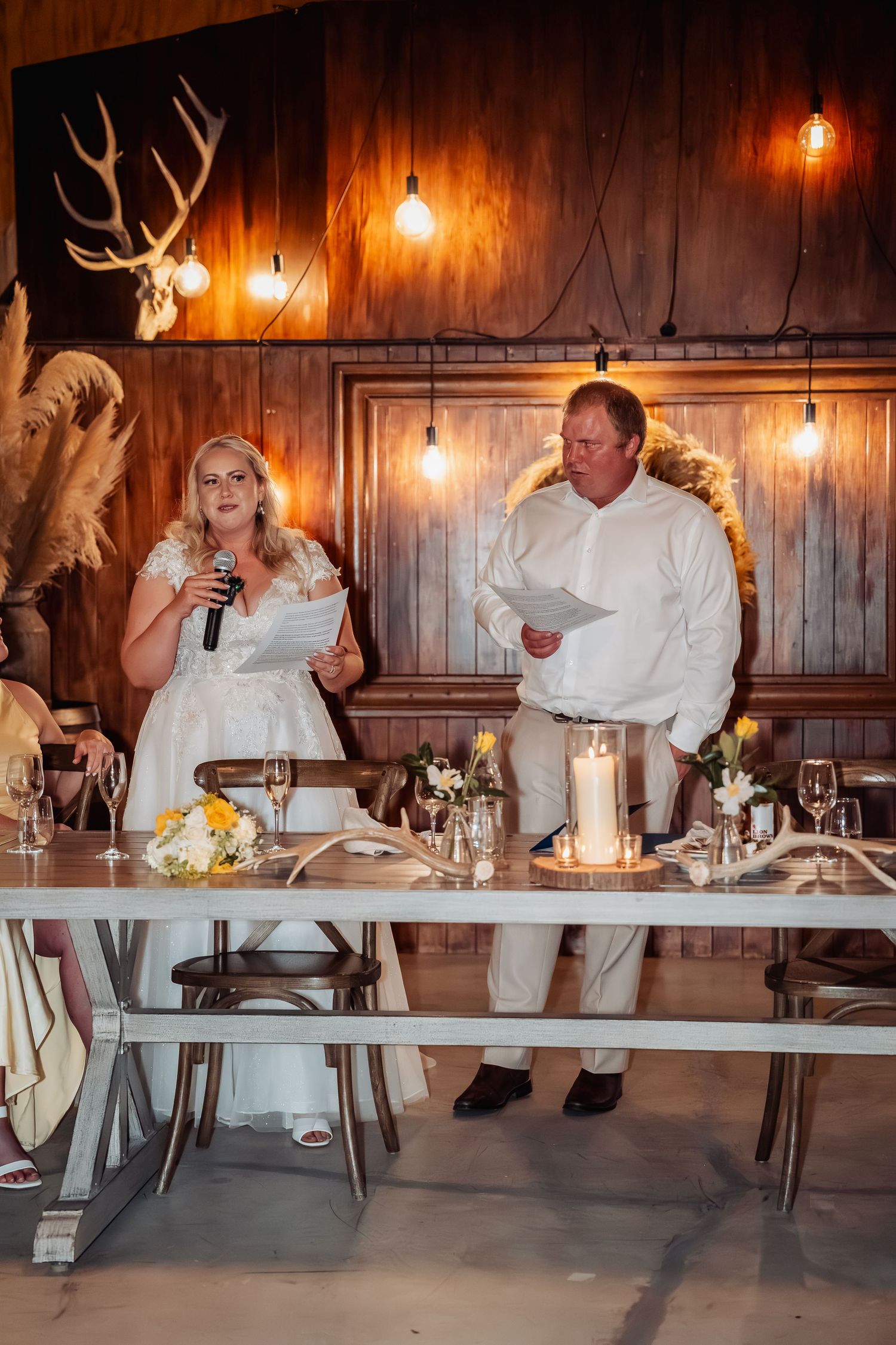 Bride and groom reading vows at rustic barn wedding reception with warm lighting.