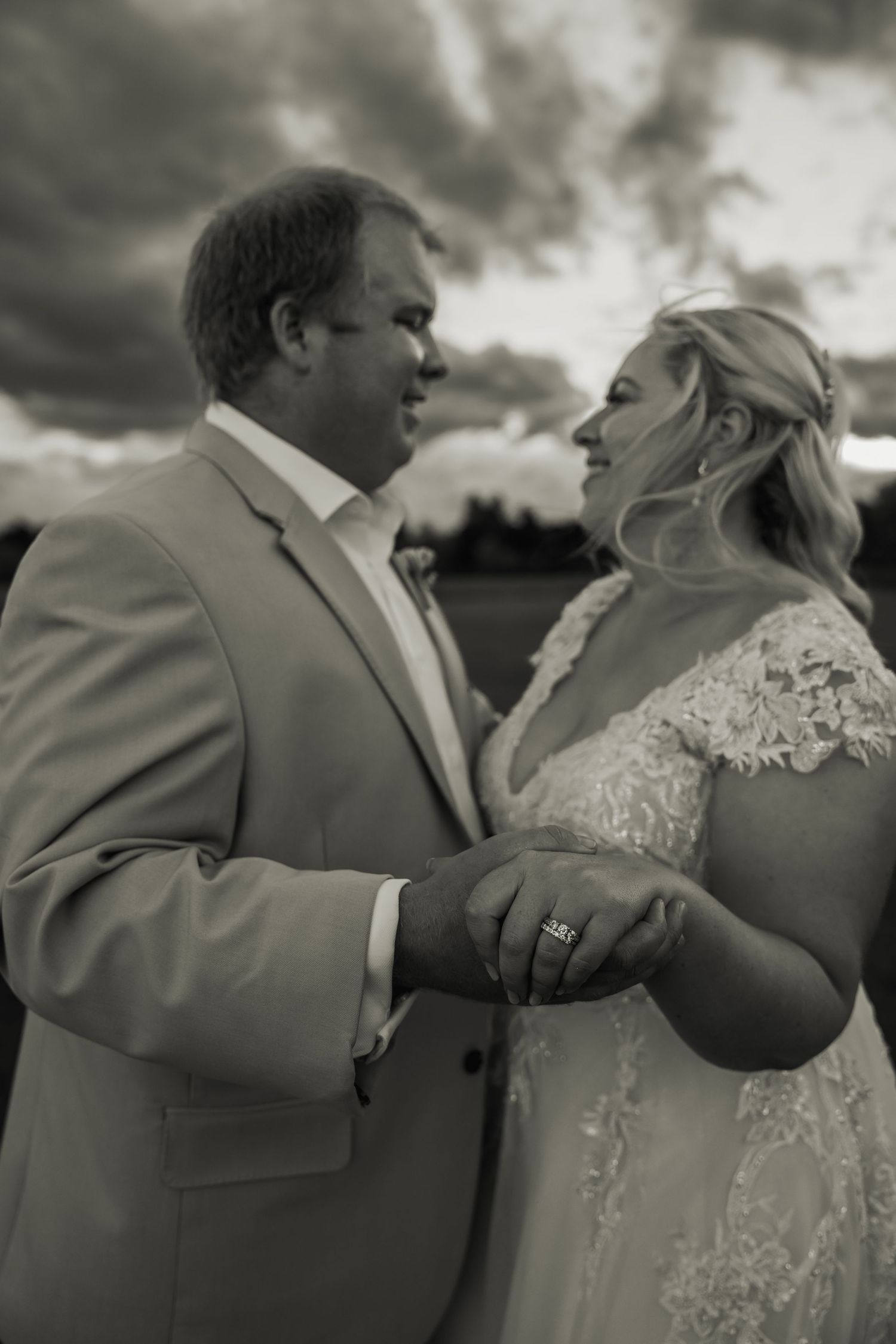 Black and white romantic portrait of bride and groom holding hands and gazing at each other outdoors.