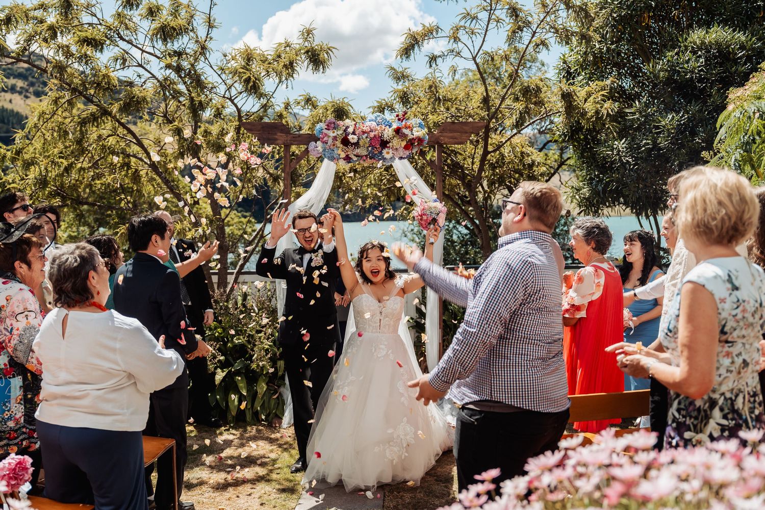 Bride and groom celebrate with confetti as guests cheer during outdoor wedding ceremony exit.