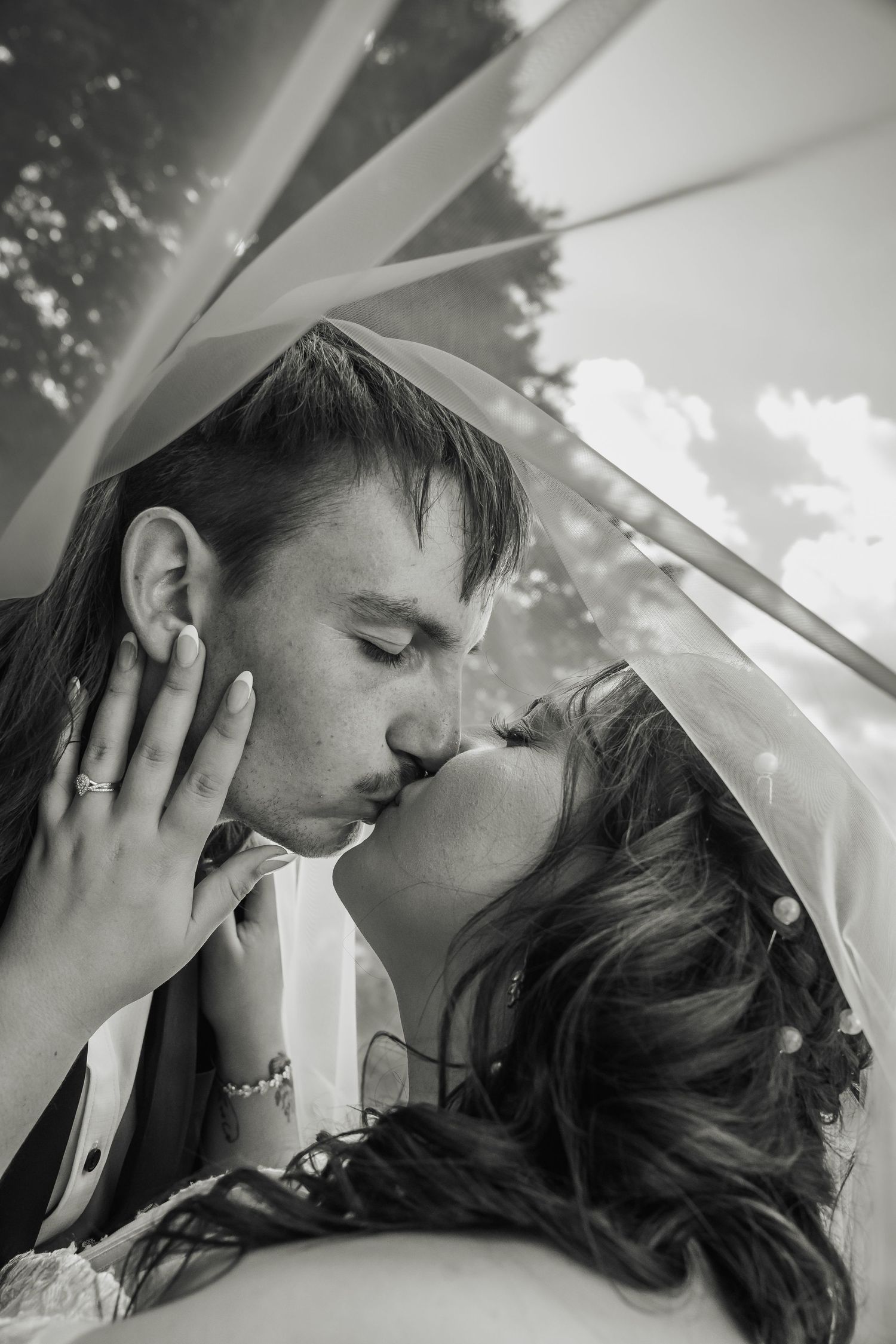Black and white close-up of bride and groom sharing a romantic kiss beneath the wedding veil.