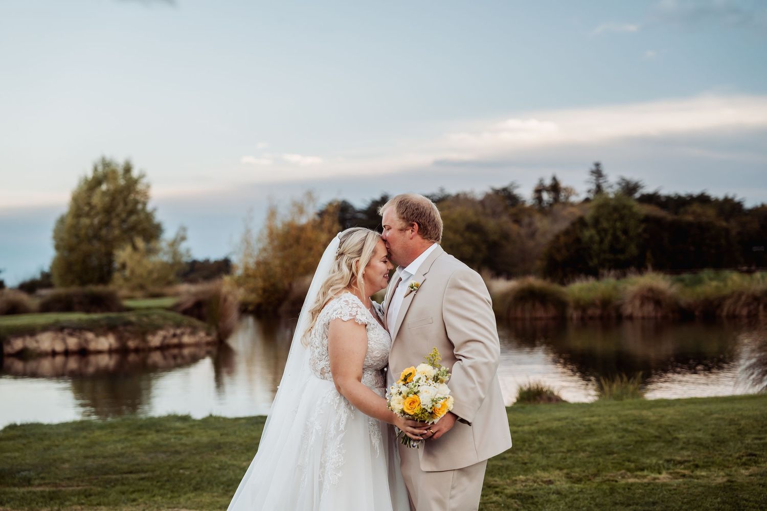 Bride and groom share a kiss near a pond at golden hour after wedding.