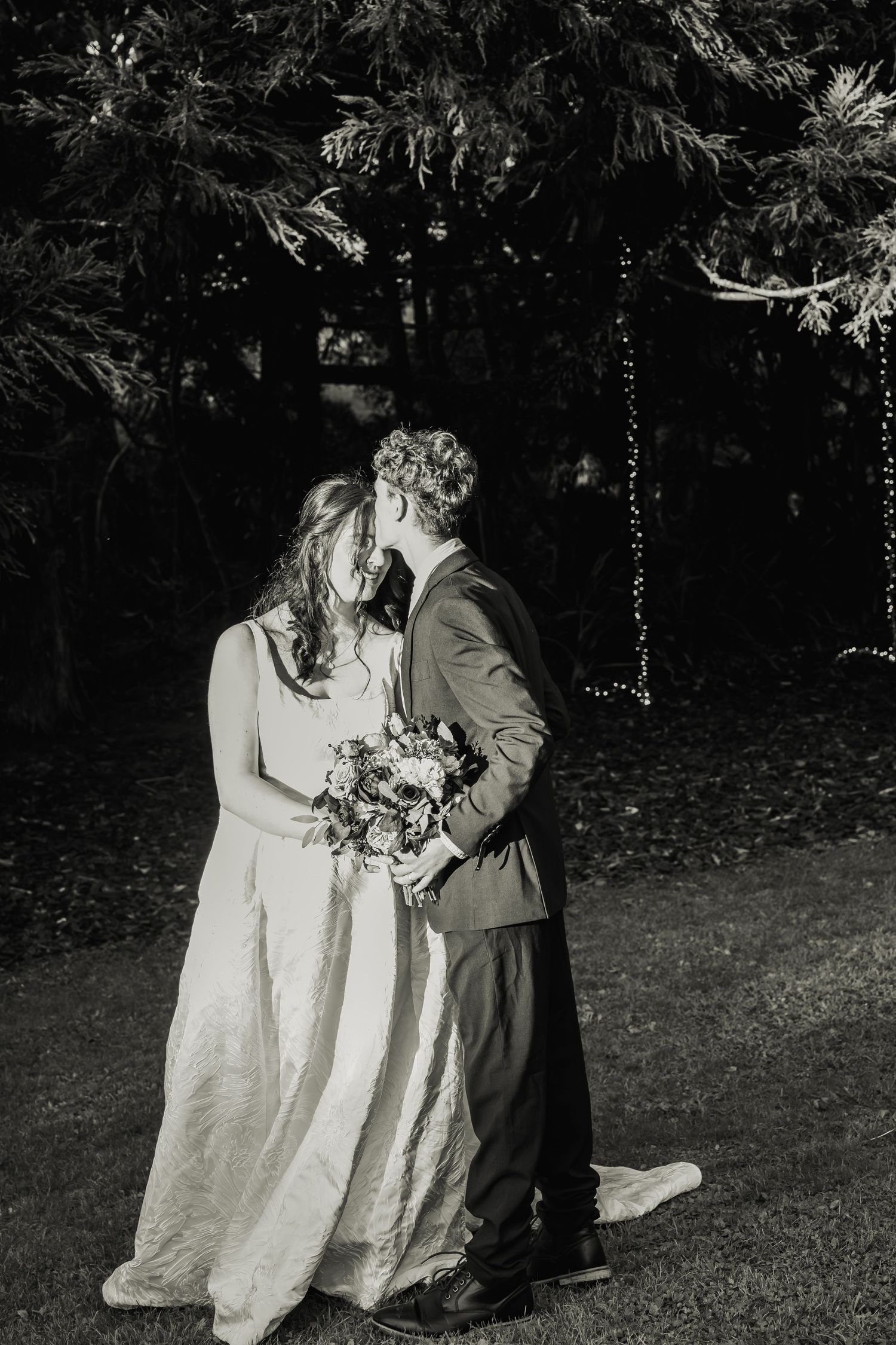 Black and white photo of bride and groom sharing a kiss outdoors at night.