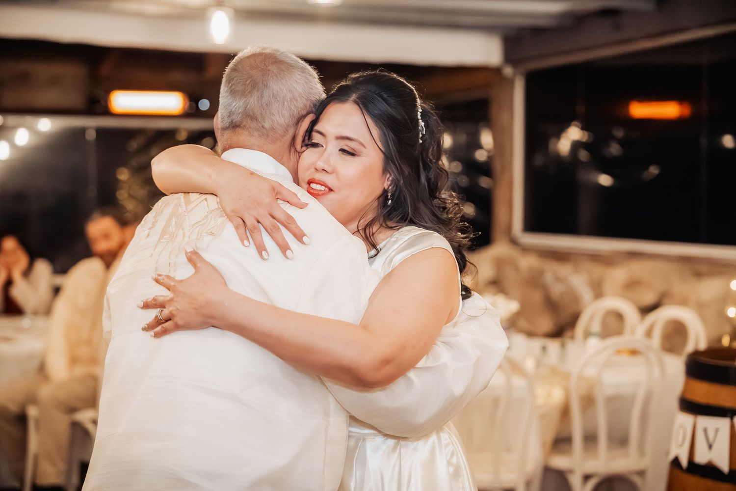 Wedding couple embraces on the dance floor surrounded by warm lighting and reception decorations.