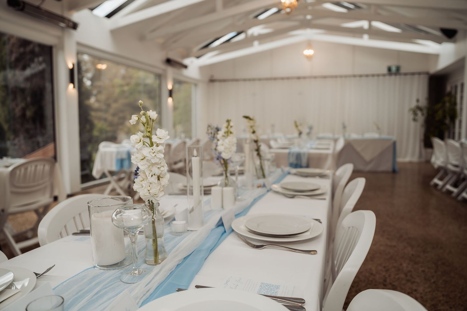 An elegant wedding reception table setting with blue accents and white place settings in a bright venue.