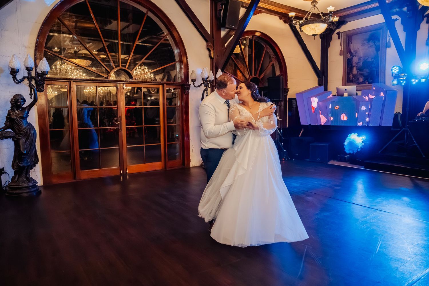 Wedding reception venue with dramatic blue lighting and elegant arched windows.