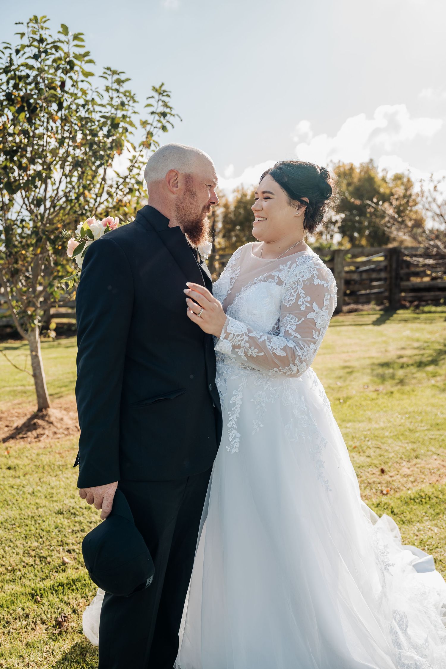 Intimate outdoor wedding portrait with couple sharing joyful moment against pastoral backdrop.