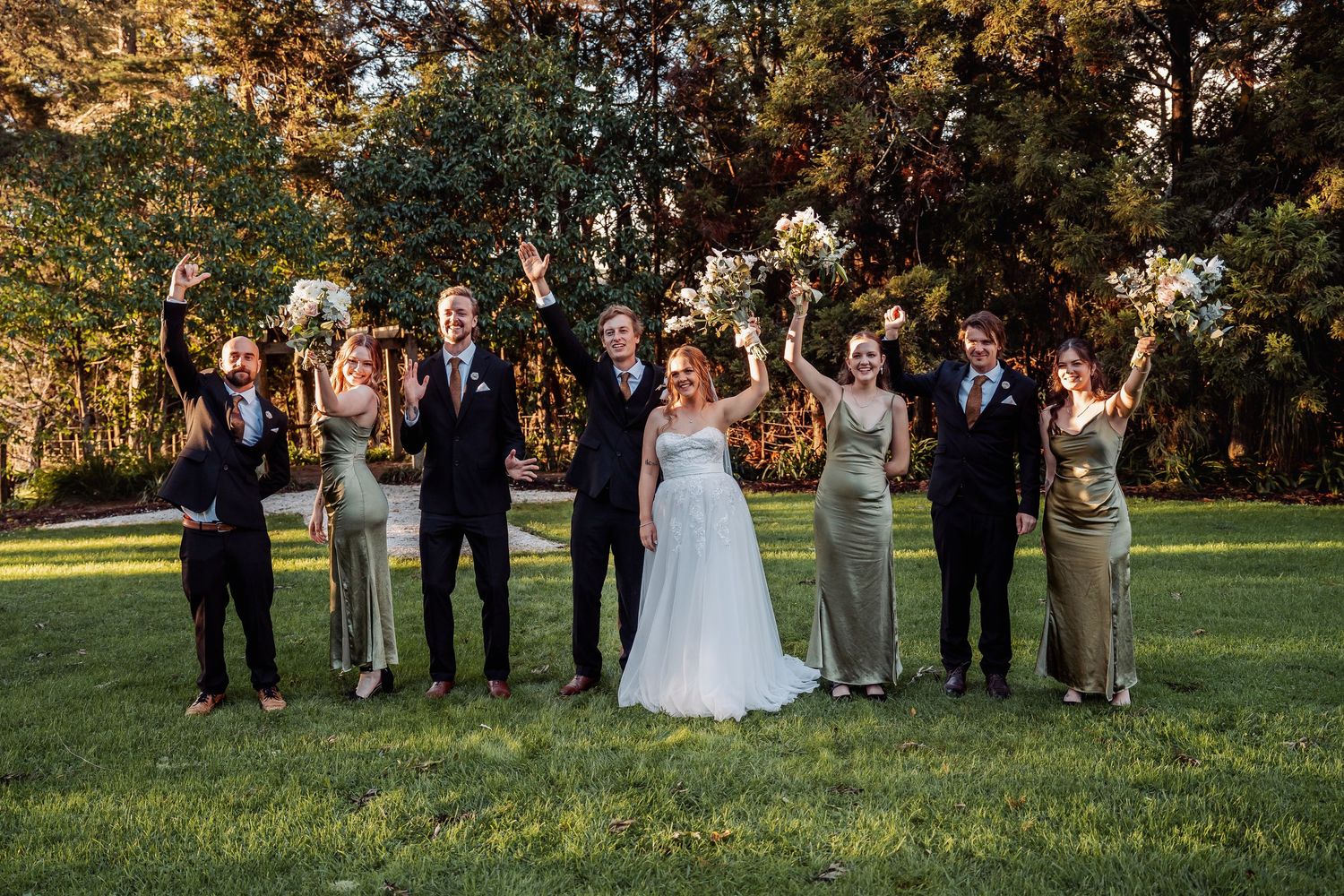 Wedding party poses outdoors with raised glasses for a celebratory toast against an autumn backdrop.