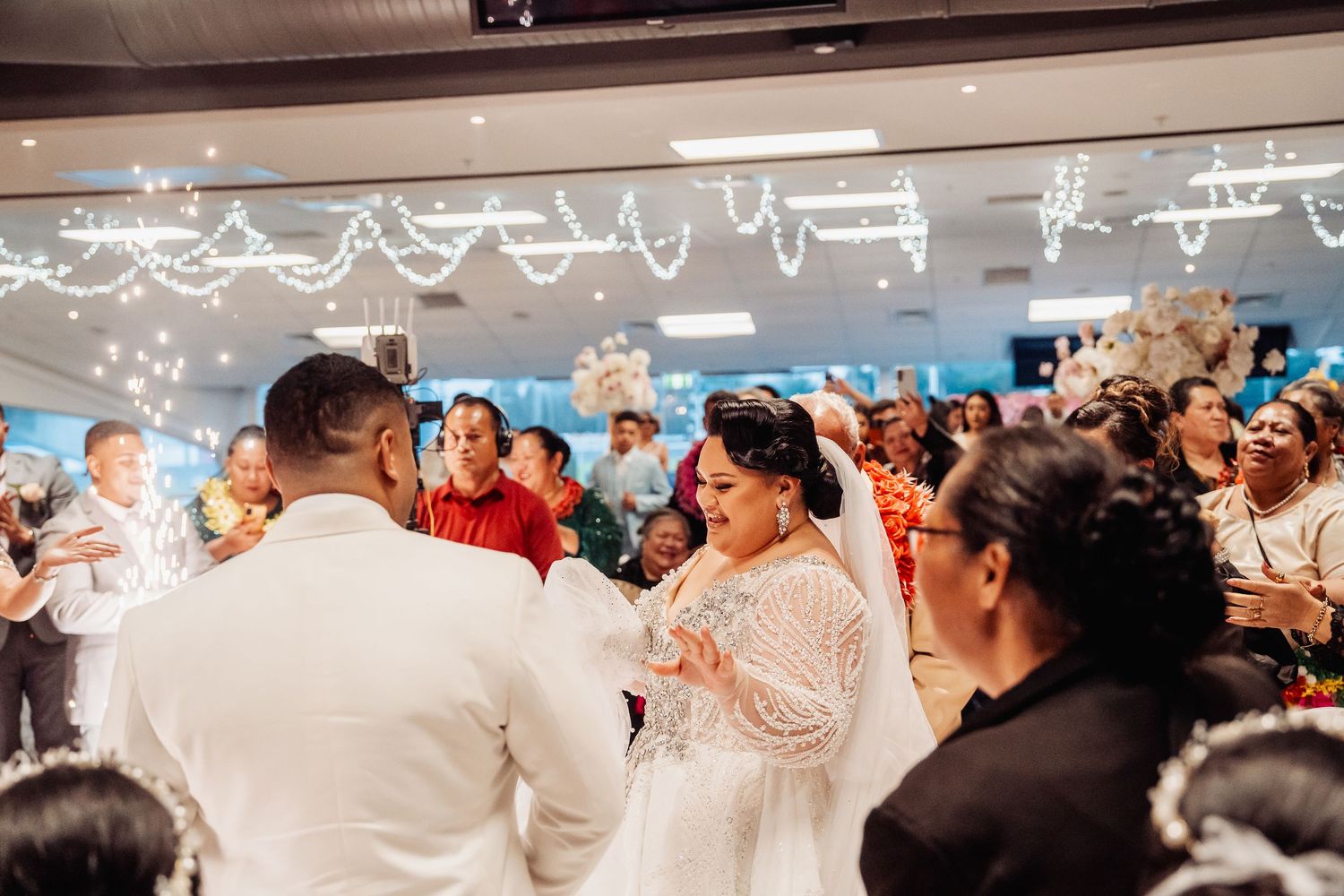 Festive reception hall decorated with string lights and filled with wedding guests.