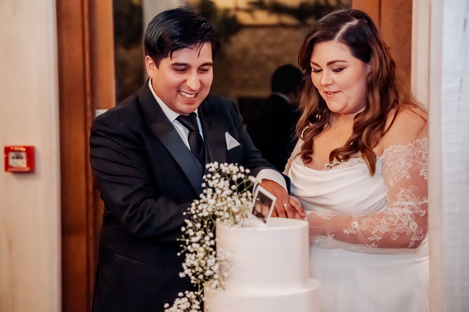 Newlywed couple cutting their elegant white wedding cake decorated with baby's breath flowers at their reception.