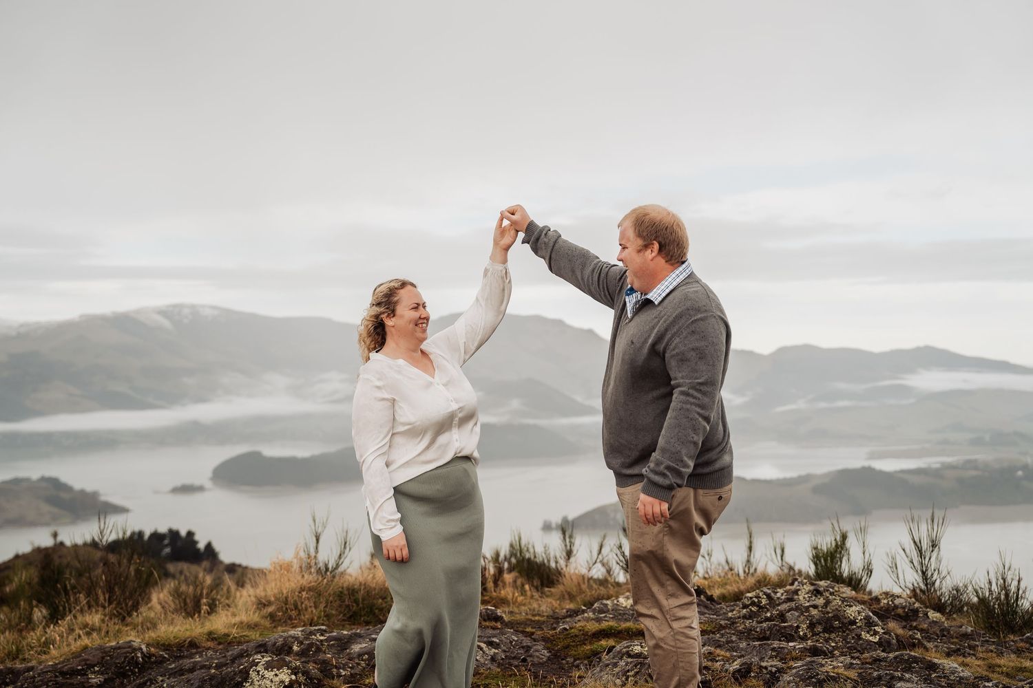 Two people embrace and dance on a misty mountaintop during a romantic outdoor moment in nature.