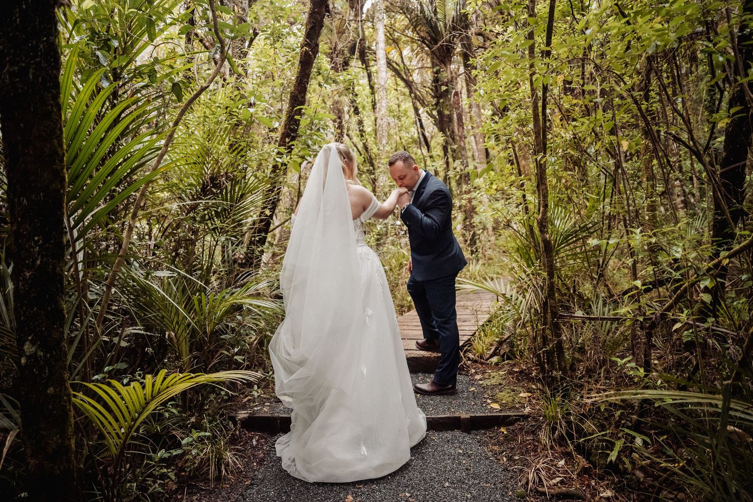 A couple shares a moment on a forest path surrounded by native ferns and trees.