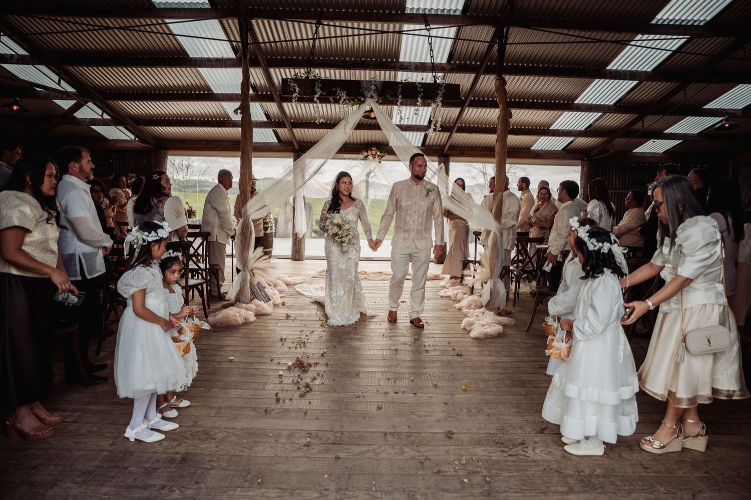 Wedding ceremony guests seated in rows inside a rustic barn venue with natural lighting.