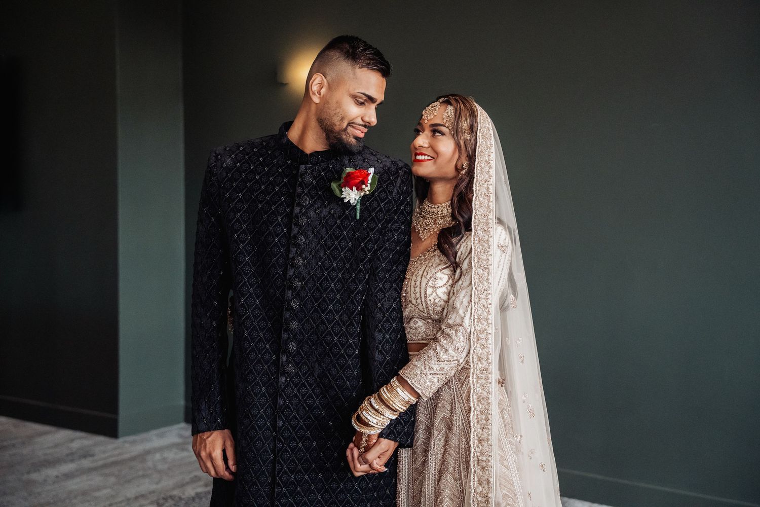 Romantic couple embrace during wedding photoshoot against moody dark backdrop.