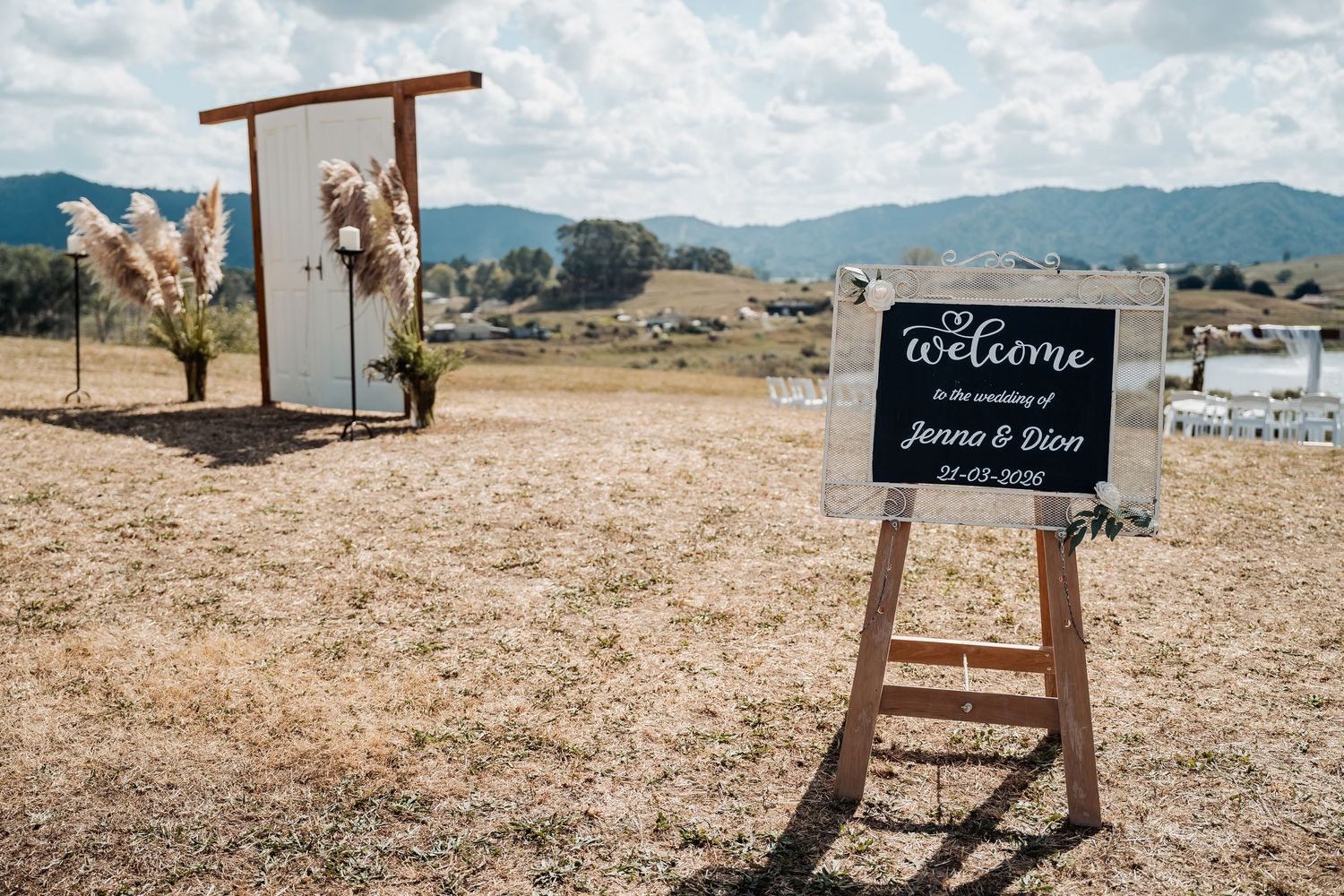 Rustic outdoor wedding welcome sign for Jenna and Dion with arch and mountains in background.