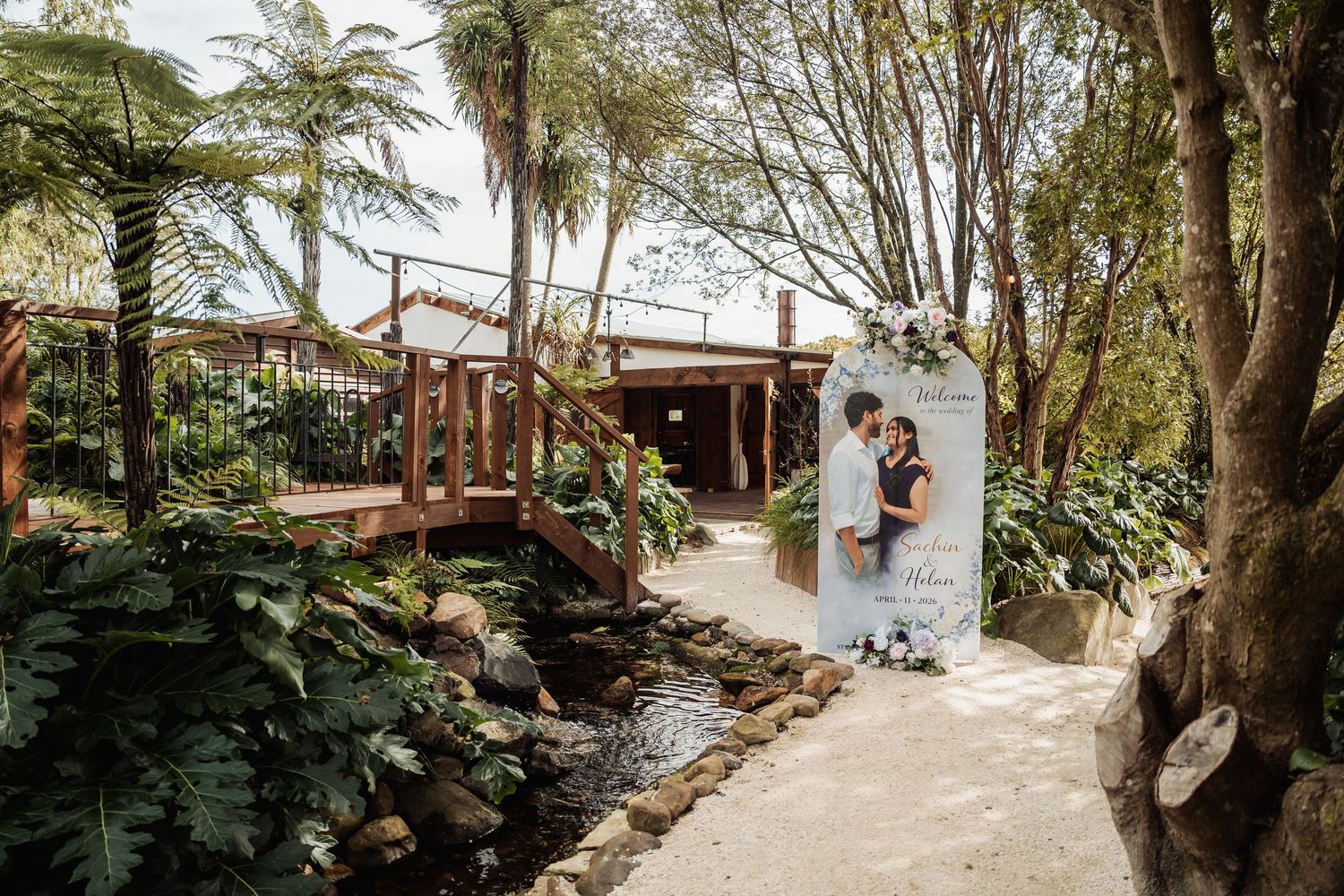 Lush tropical garden wedding venue with a romantic couple portrait sign along a stone path surrounded by greenery.
