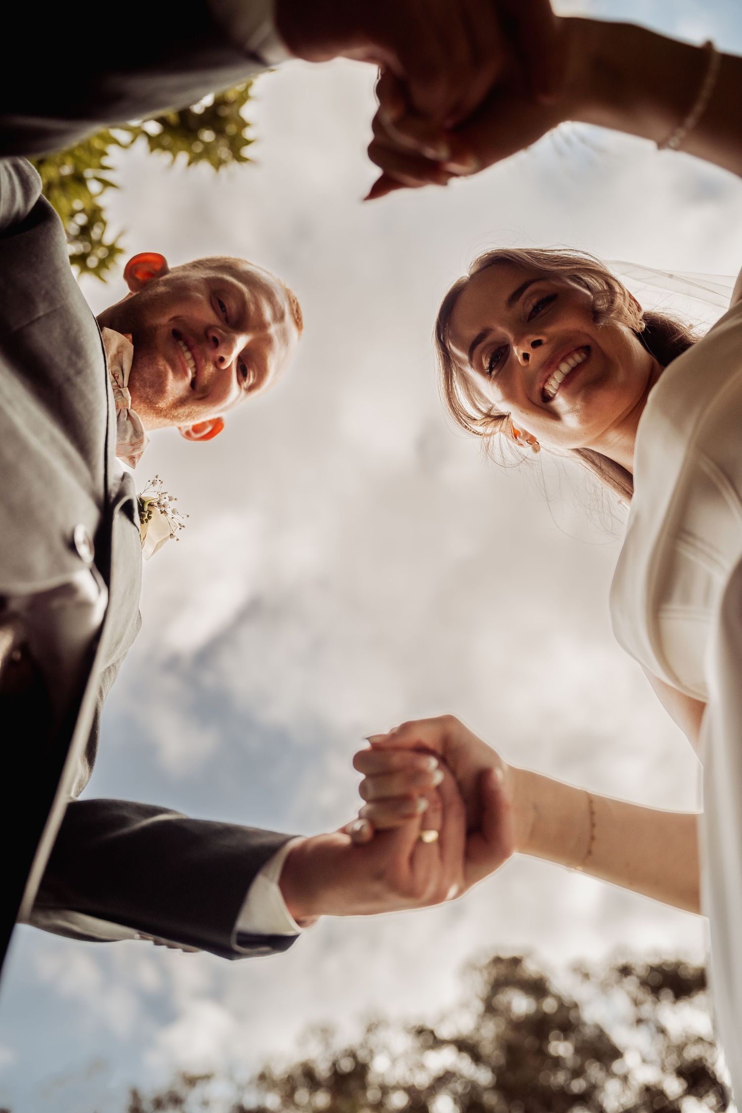 Low angle view of smiling bride and groom holding hands under sunny sky at wedding ceremony.