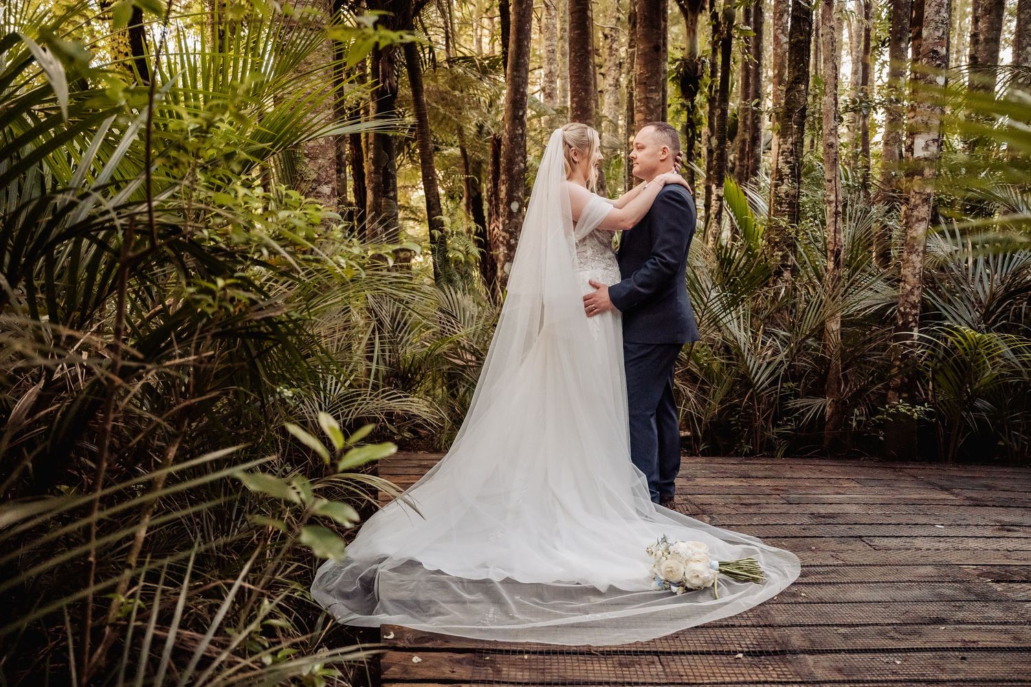 Newlyweds share romantic moments on a wooden walkway surrounded by forest greenery.