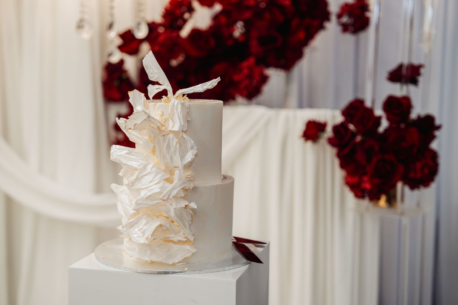 White wedding cake decorated with red floral arrangements and delicate white details.