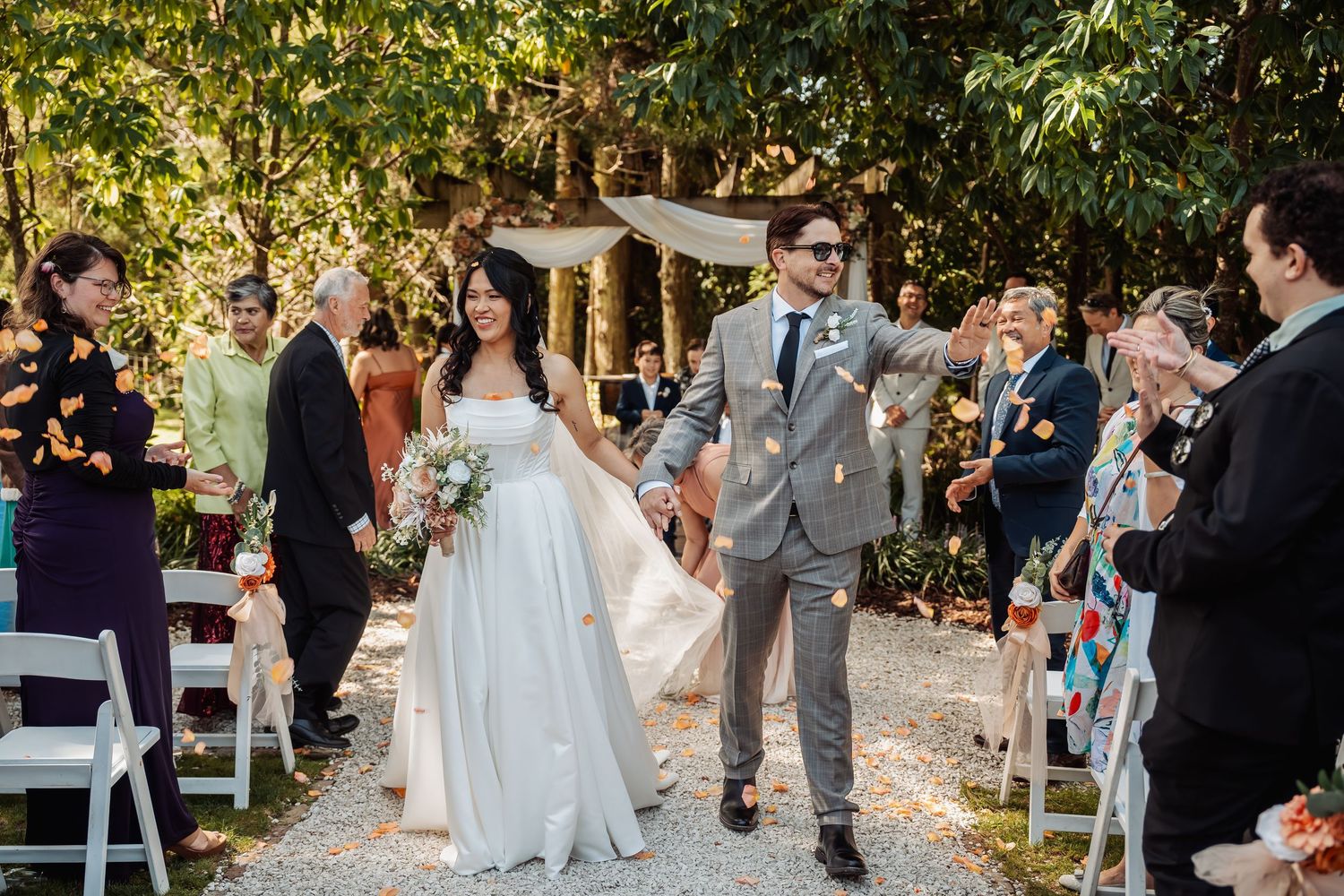 Newlyweds walk joyfully down the aisle as guests toss colorful flower petals in celebration.