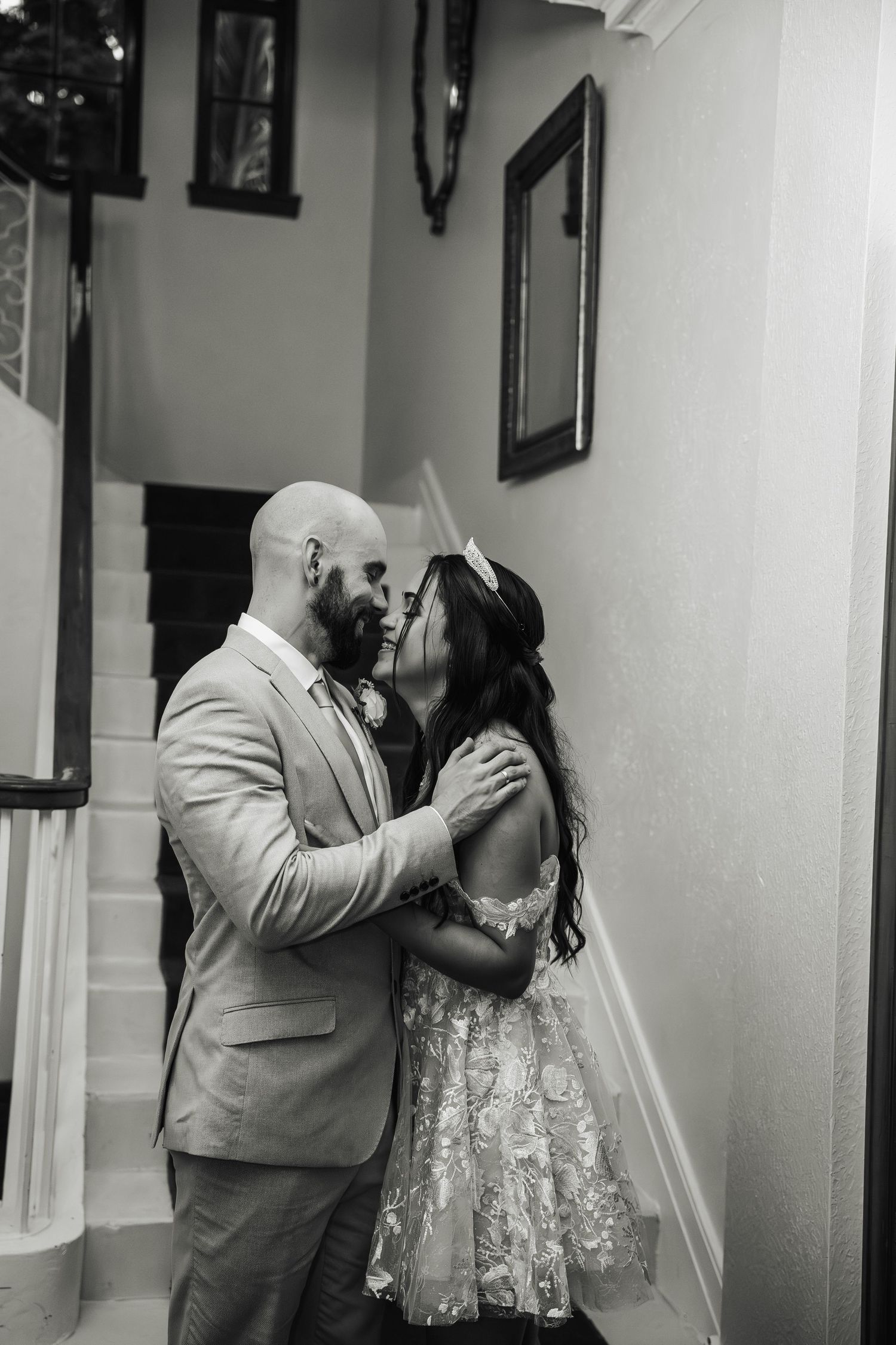 Black and white romantic photo of bride and groom kissing on staircase inside elegant venue.