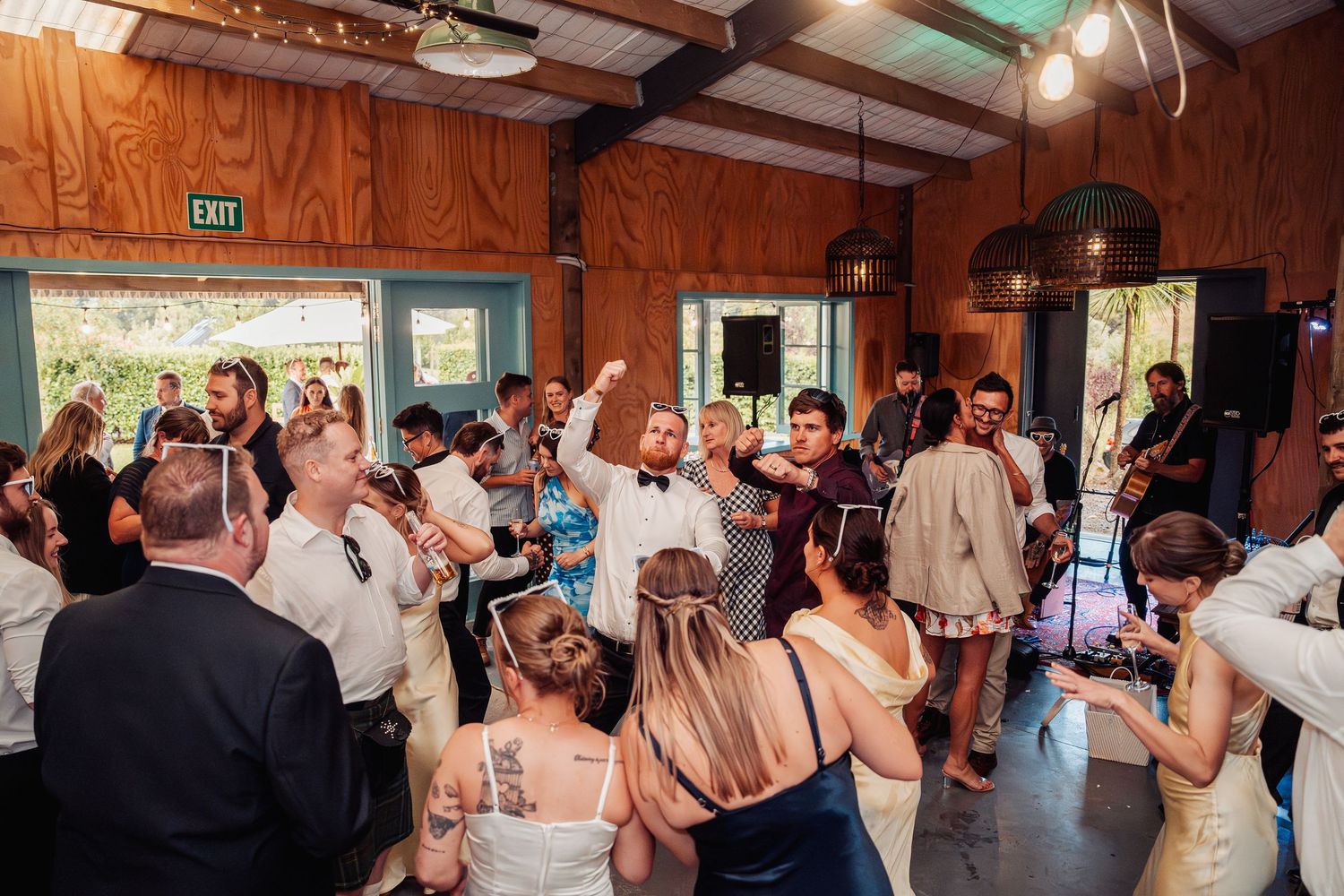 Energetic wedding reception dance floor packed with guests celebrating inside a wooden venue.