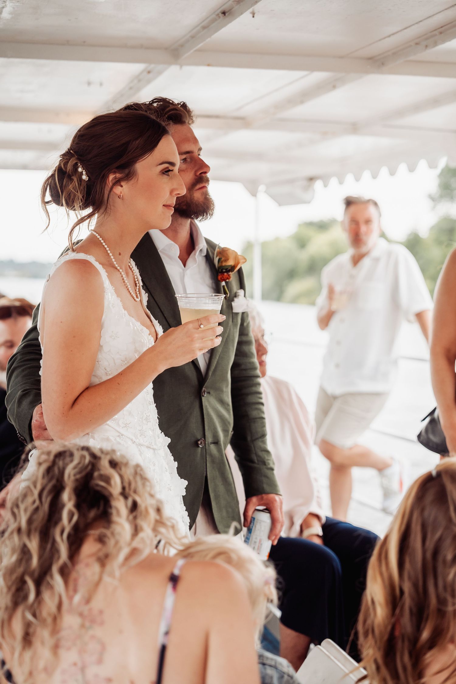 Bride and groom holding drinks and listening to speeches during outdoor tented wedding reception.