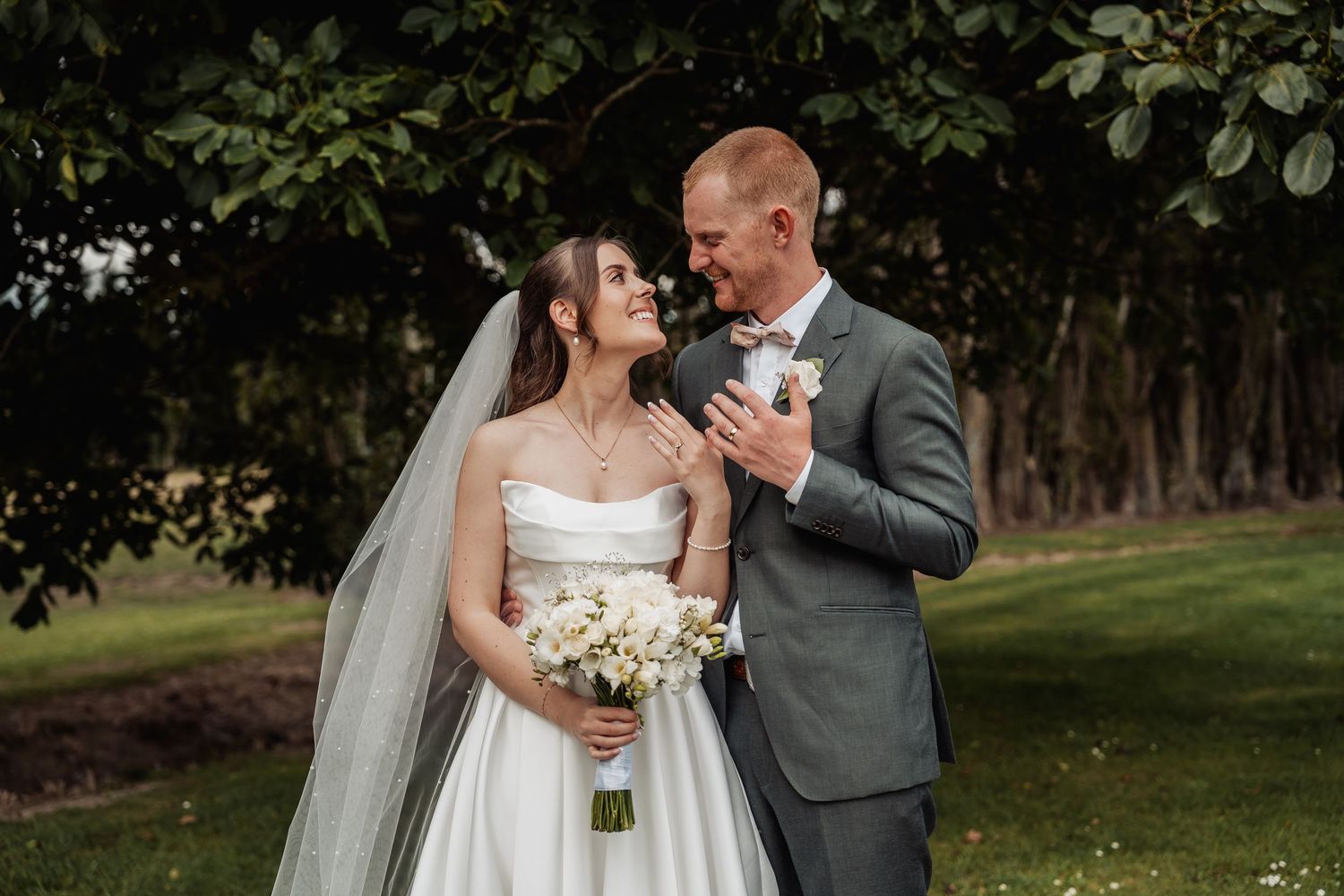Bride and groom share a tender moment in a garden, bride holding white bouquet wearing a strapless gown.