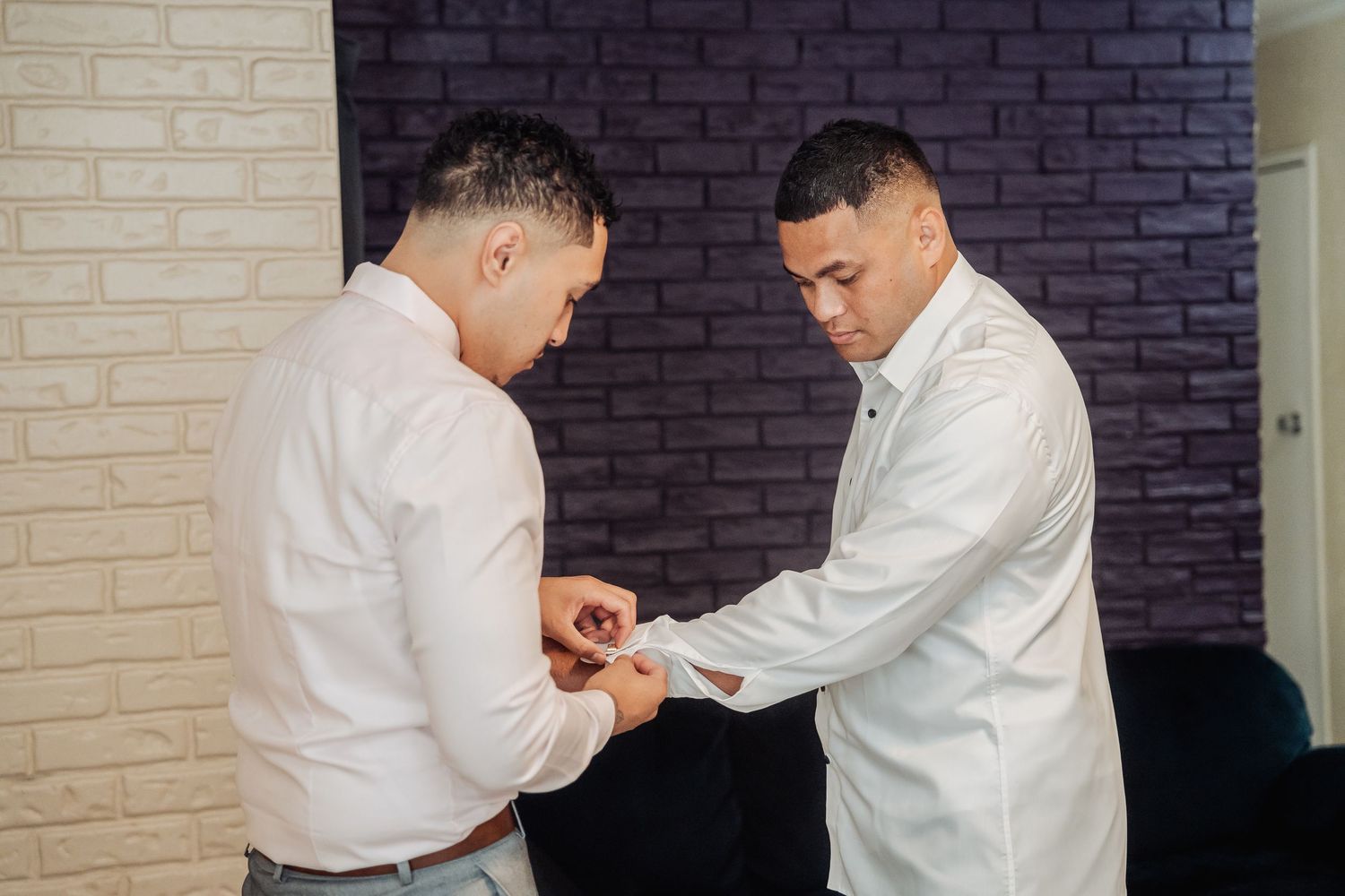Doctor adjusts a cufflink on another doctor's white medical coat sleeve while standing in a hallway.