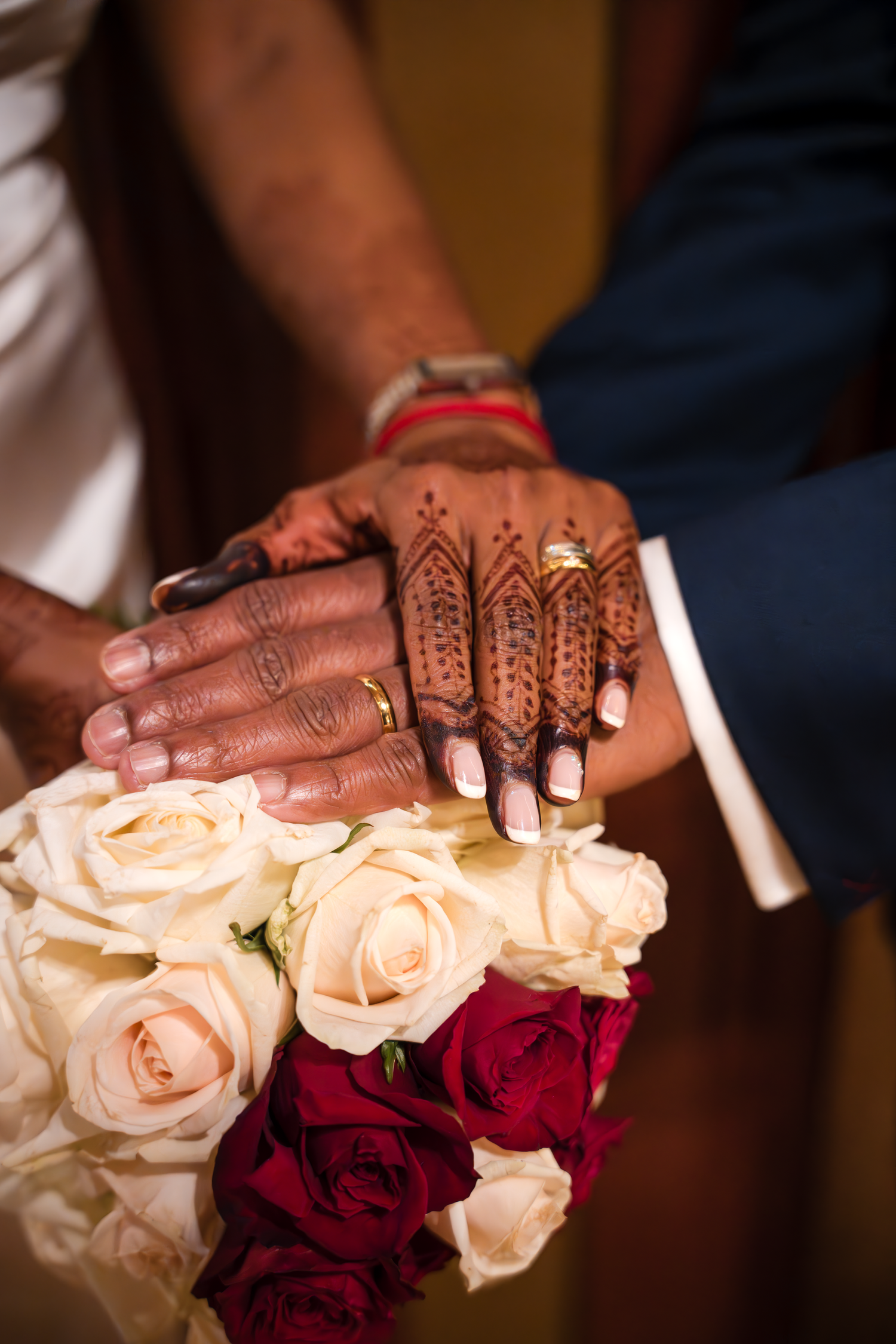 Decorated hands with henna patterns rest on a bouquet of cream and red roses.